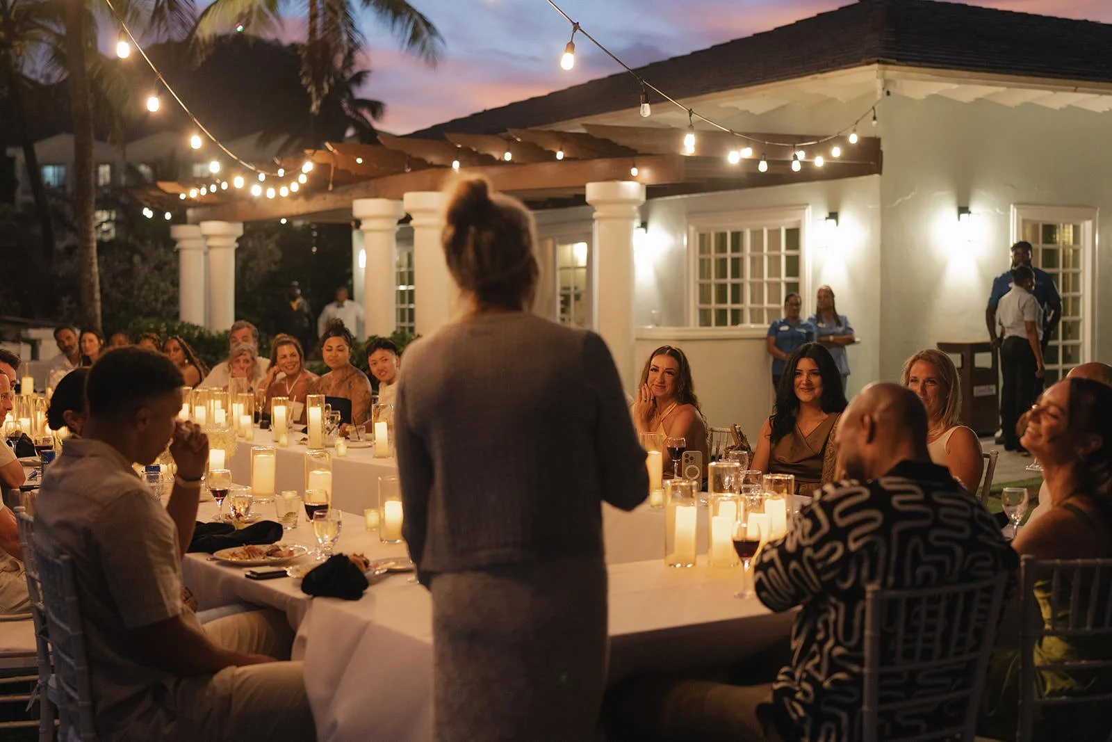 Wedding guests seated at the long welcome dinner table in St. Lucia, with a small island visible on the water behind them at dusk