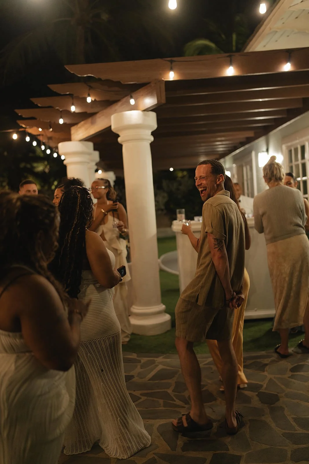 Wedding guests mingling on a covered patio strung with lights at night, St. Lucia