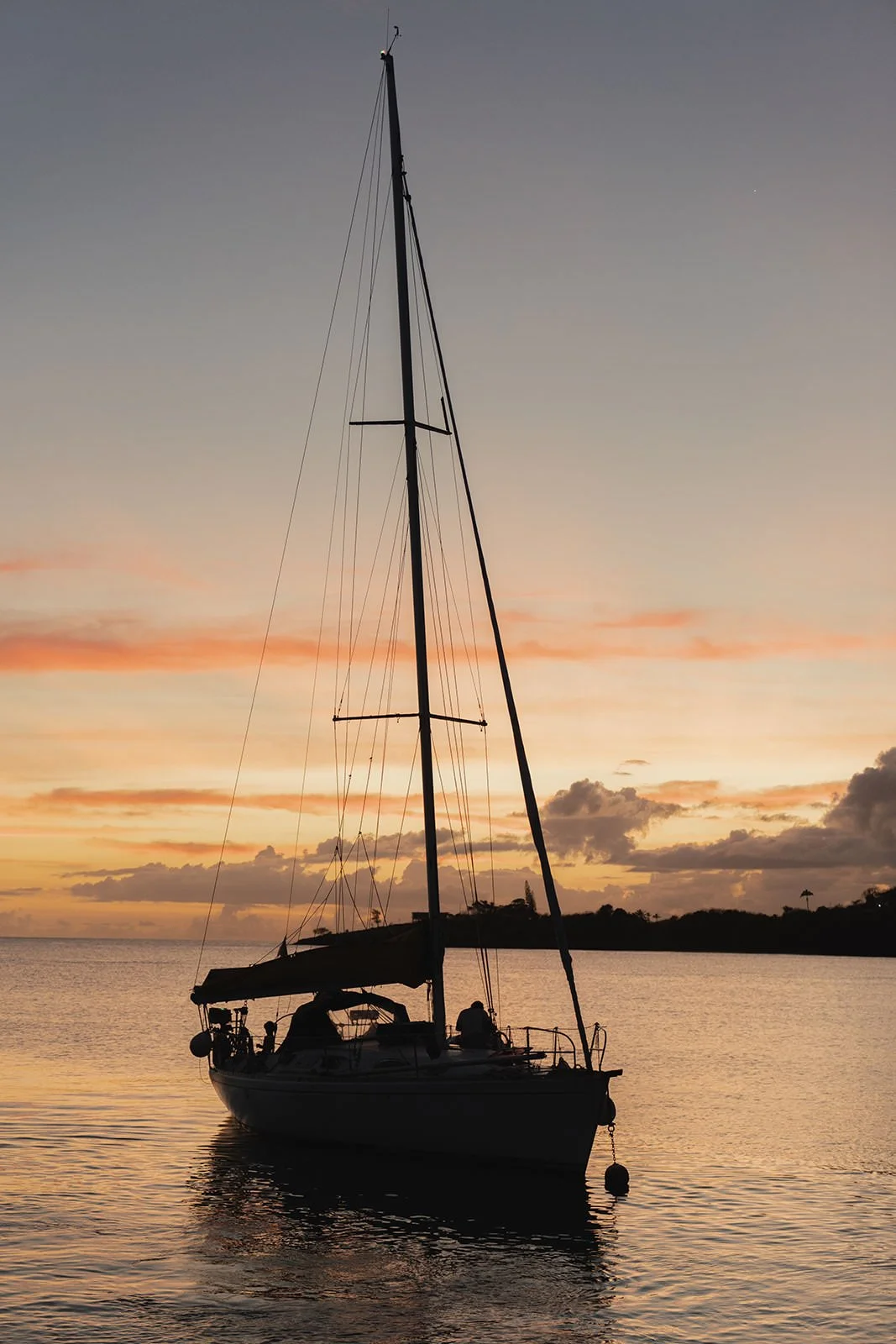 Sailboat silhouetted against an orange and pink St. Lucia sunset sky, anchored offshore during the wedding weekend catamaran excursion