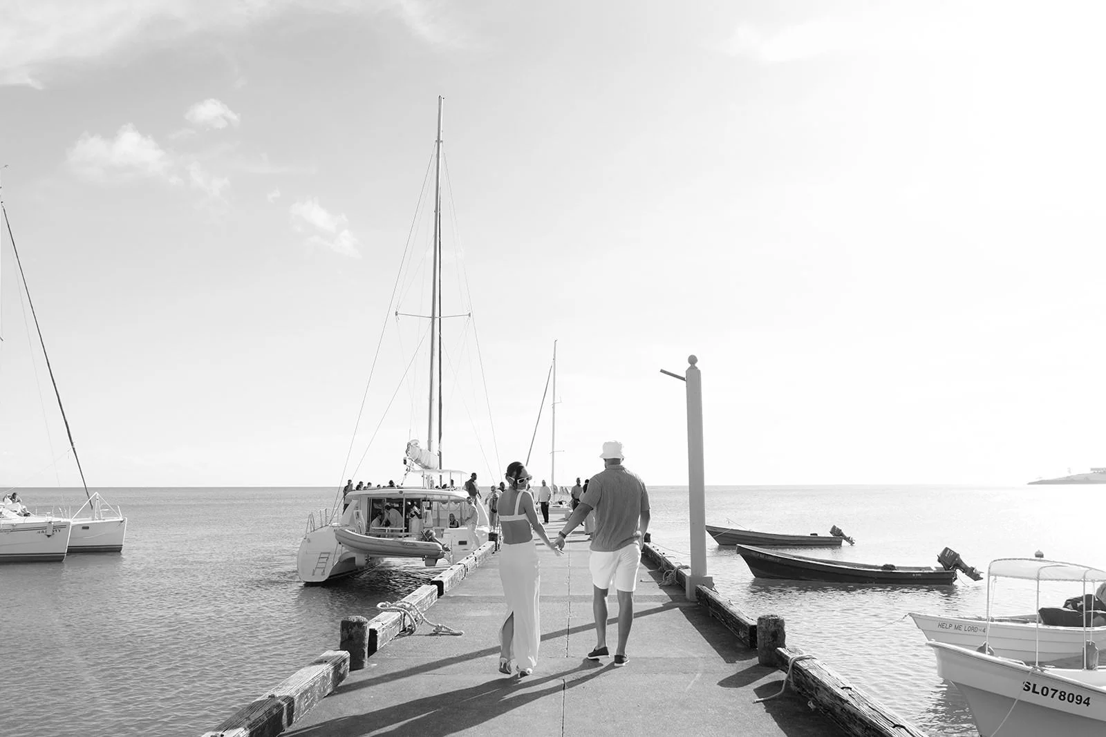 Person walking along a dock in a St. Lucia harbor lined with sailboats, black-and-white toned photo from the wedding weekend catamaran excursion
