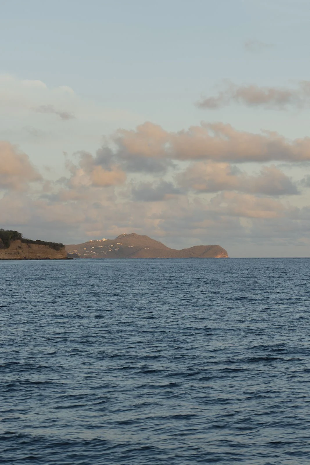 View of a distant St. Lucia island coastline under soft clouds at dusk, seen from the catamaran during the sailing excursion