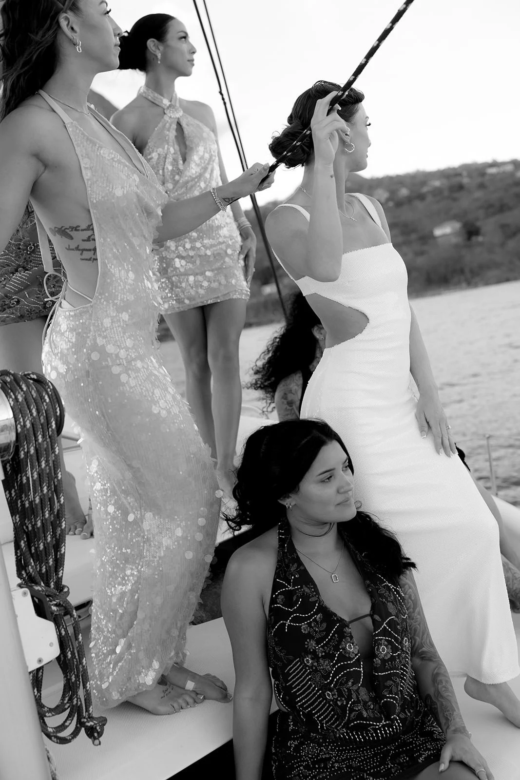 Black-and-white photo of the bride and bridesmaids standing together at the catamaran's mast, St. Lucia coastline in the background