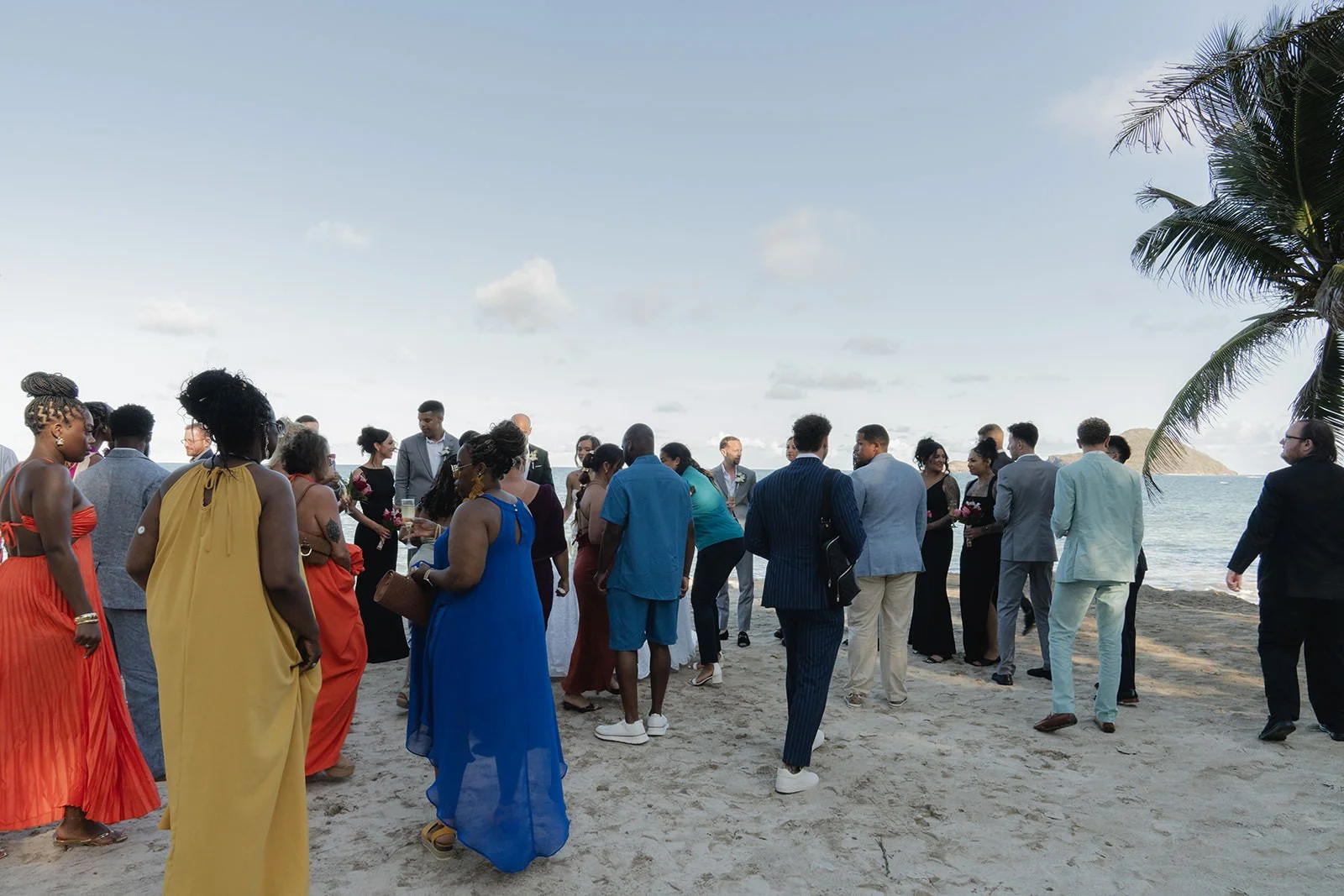 Wedding guests in colorful attire gathered on the beach at Coconut Bay Beach Resort, watching the St. Lucia wedding ceremony