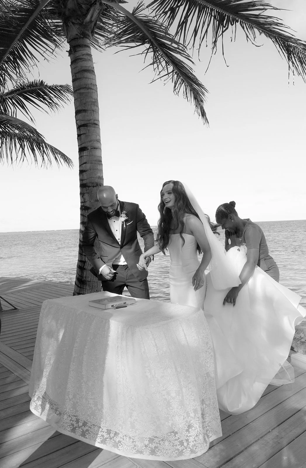 Black-and-white photo of the bride and groom signing their marriage certificate at a beachside table under palm trees in St. Lucia