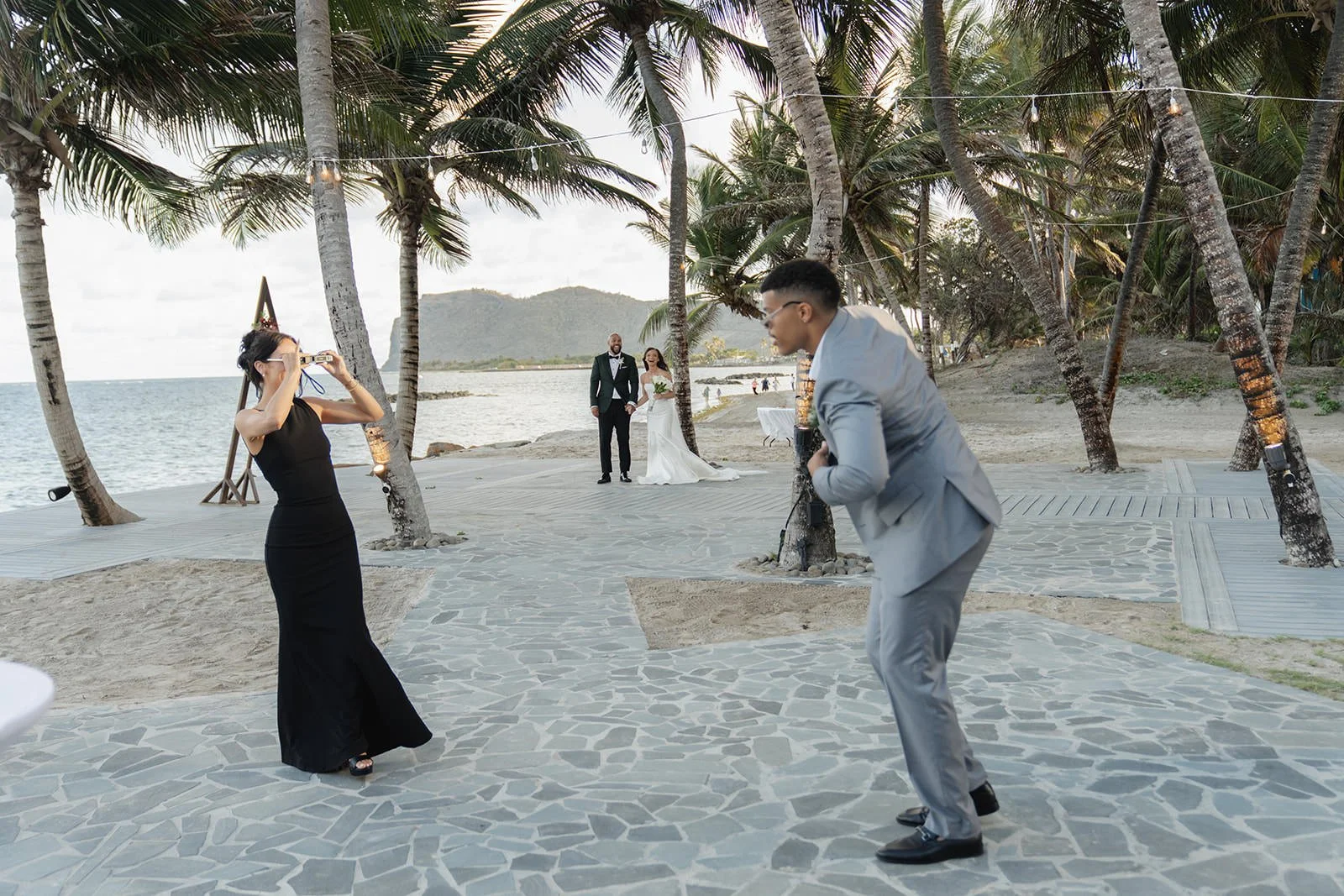 Groomsmen in gray suits and bridesmaids in black dresses posing playfully among palm trees on the St. Lucia beach