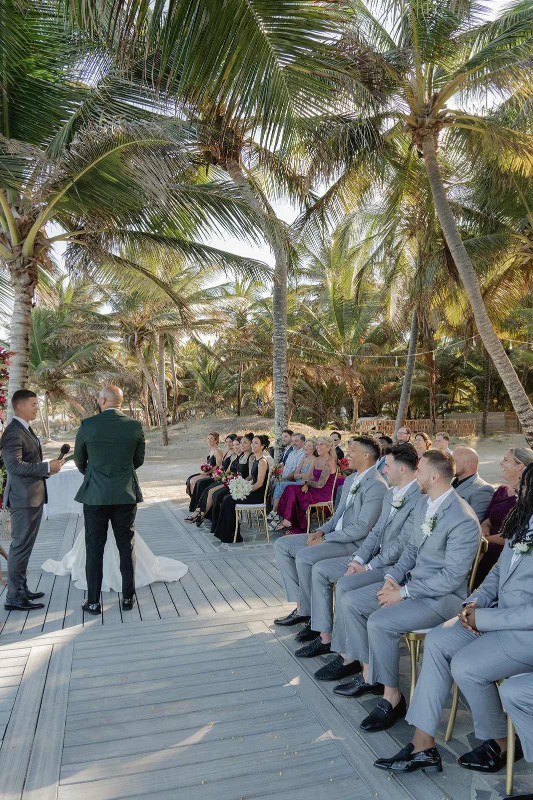 Officiant addressing groomsmen seated on a palm-shaded wooden deck during the St. Lucia beach wedding ceremony