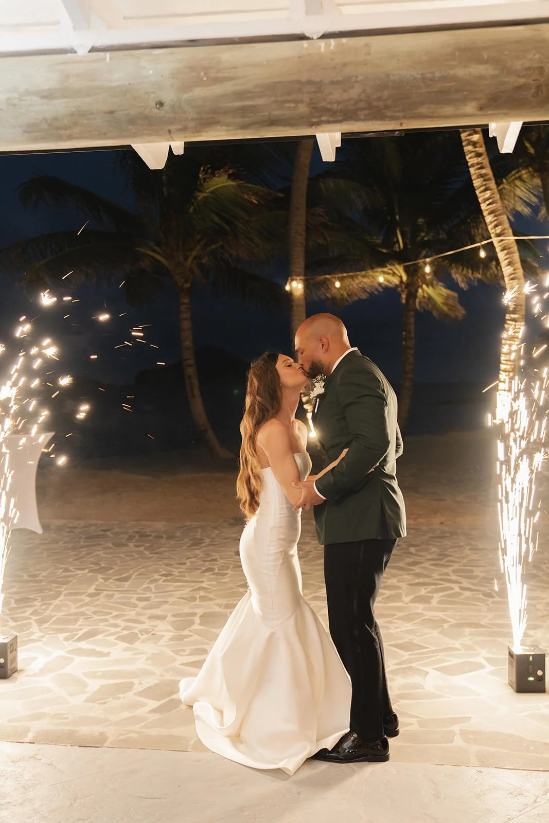 Groom and bride kissing at night under string lights during their St. Lucia wedding reception