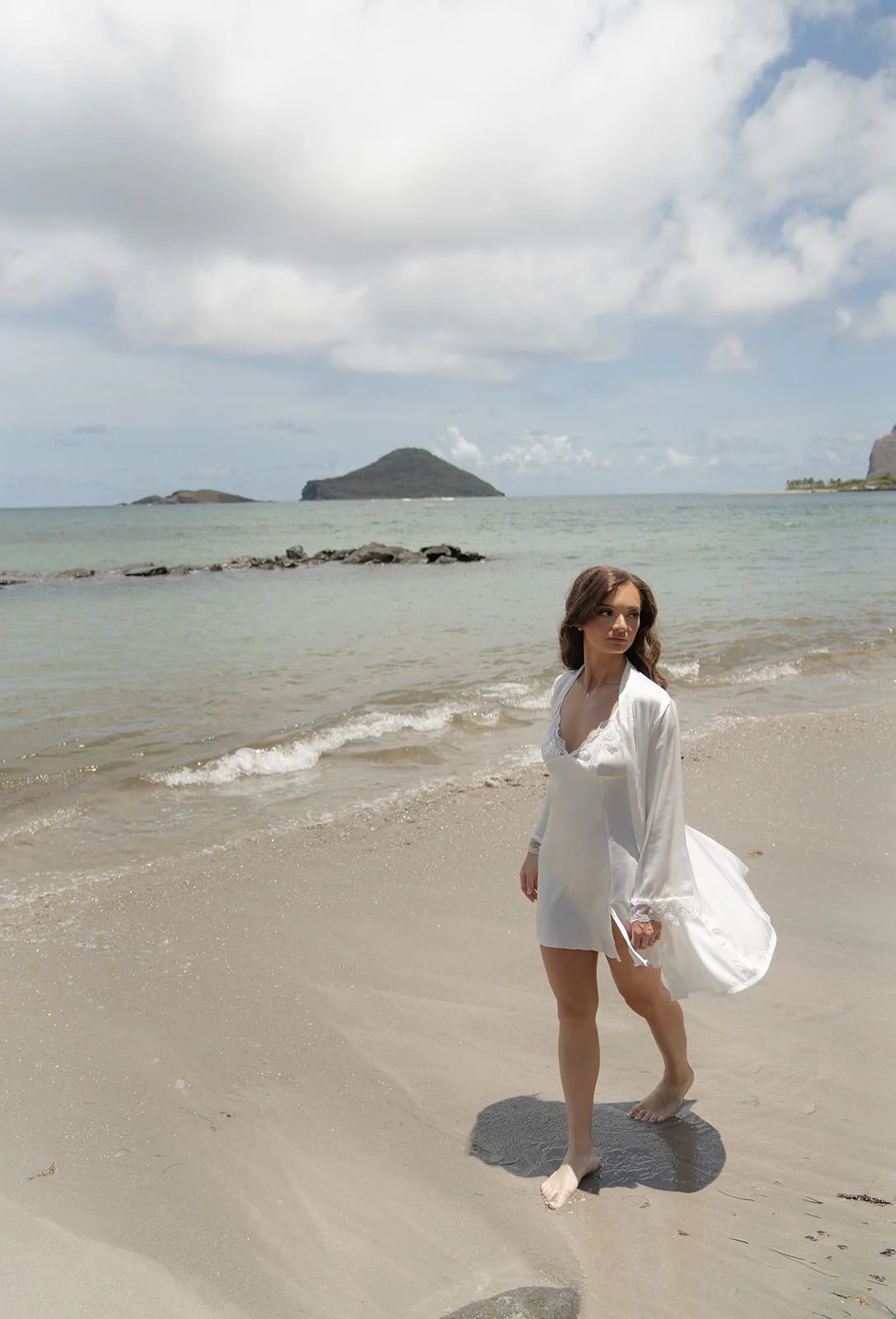Bride walking along the St. Lucia beach with a small offshore island visible under a cloudy sky