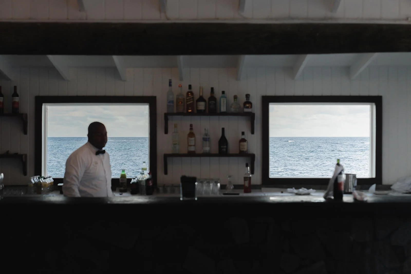 Bartender preparing drinks behind the bar at the St. Lucia wedding venue, ocean visible through the windows