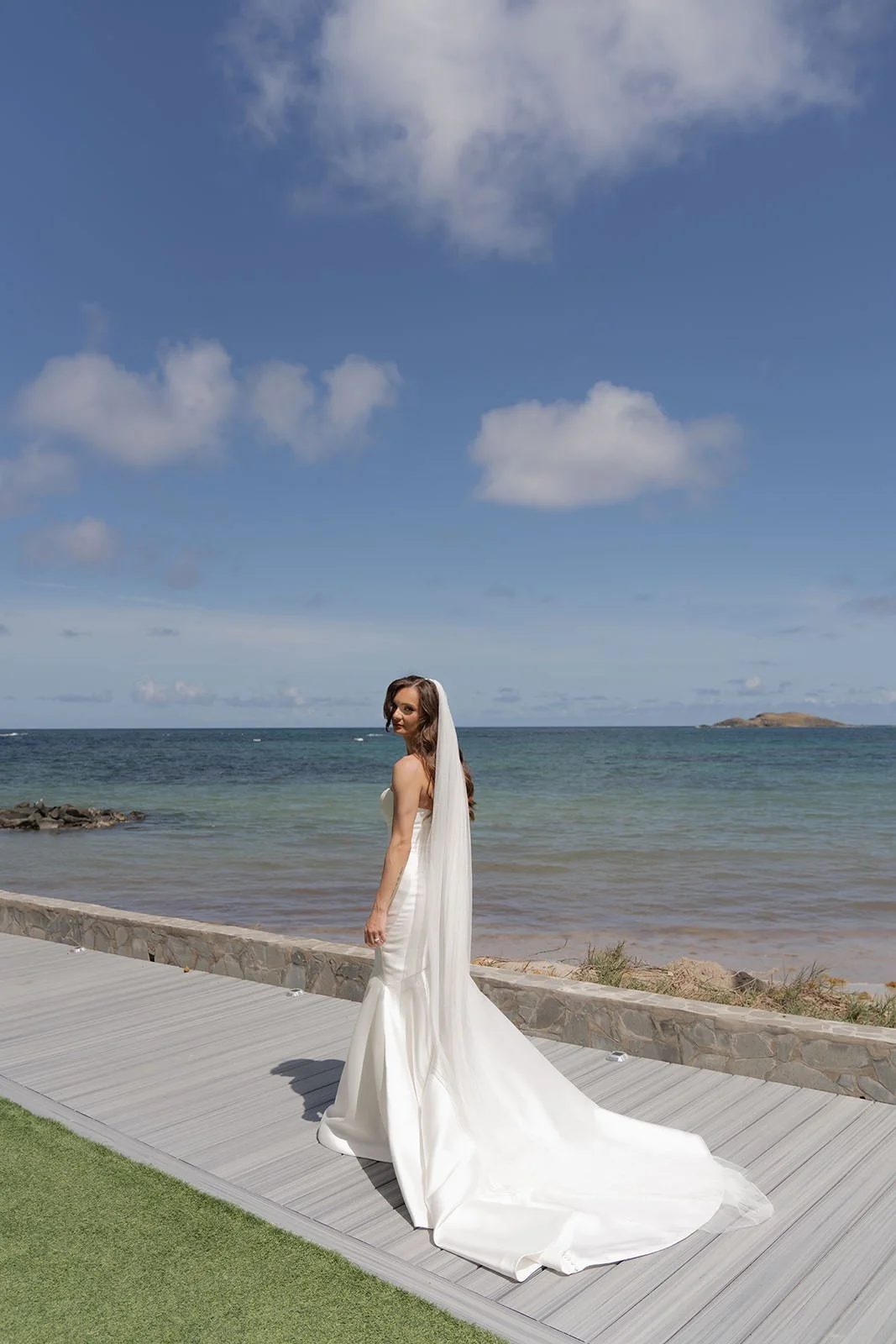 Bride standing on the boardwalk with her long veil trailing, an offshore island visible on the St. Lucia coastline