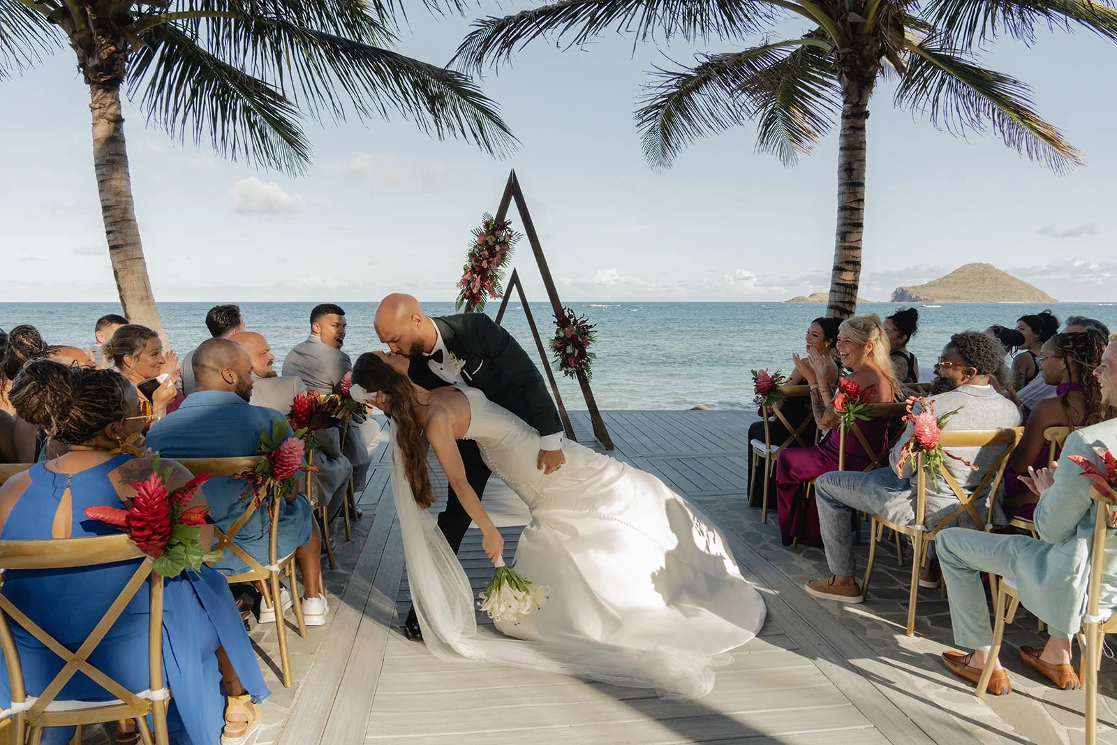 Wide view of the St. Lucia beach wedding ceremony from behind the seated guests, bride walking down the aisle toward the ocean-view arch