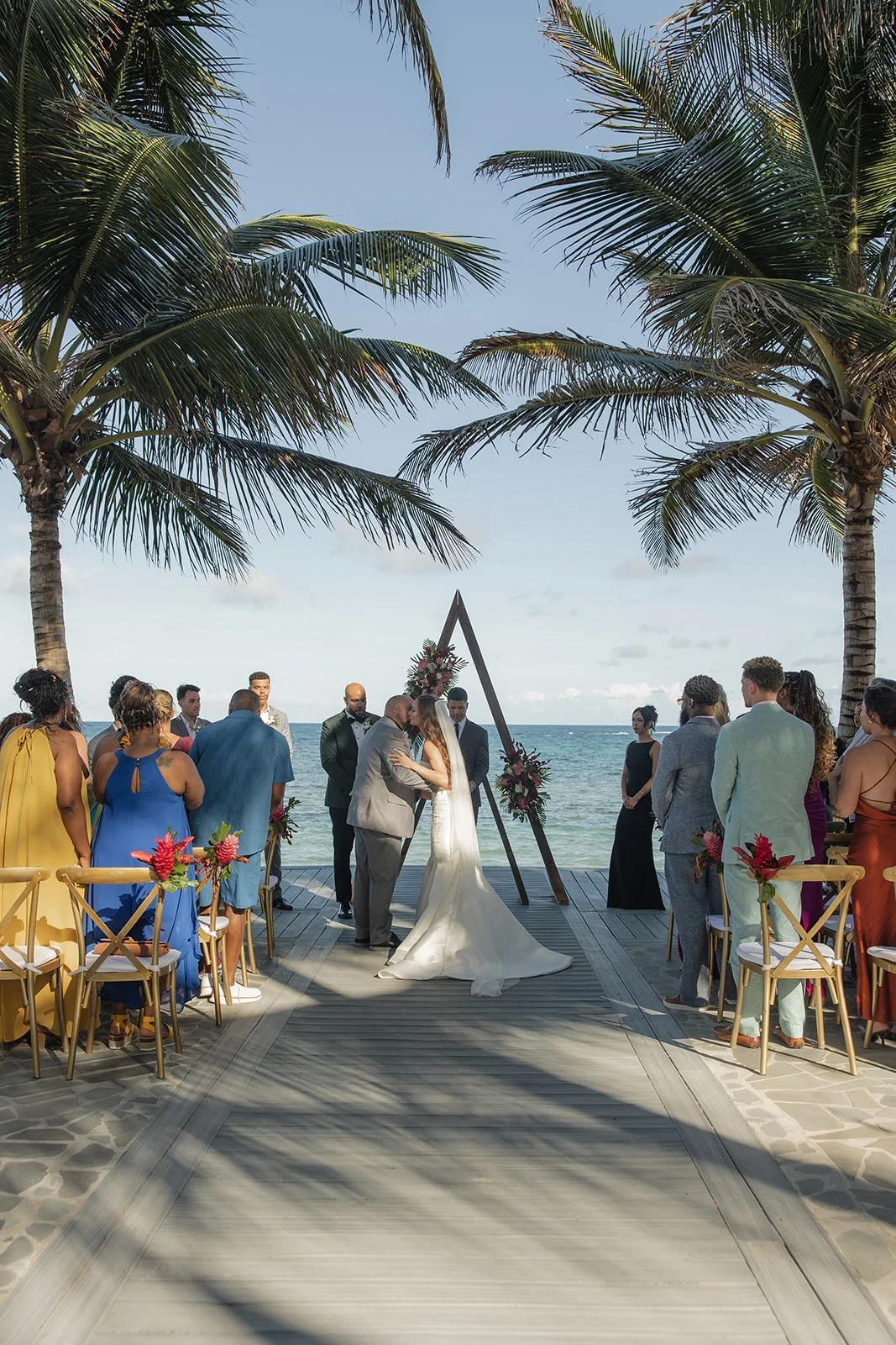 Wide view of the St. Lucia wedding ceremony aisle lined with guests in chairs beneath palm trees, leading to the triangular arch