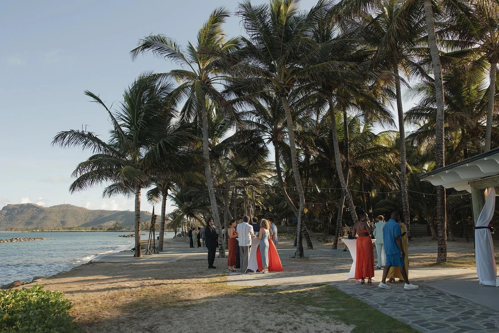 Wedding guests in colorful attire gathered along a palm-lined beach path at dusk in St. Lucia