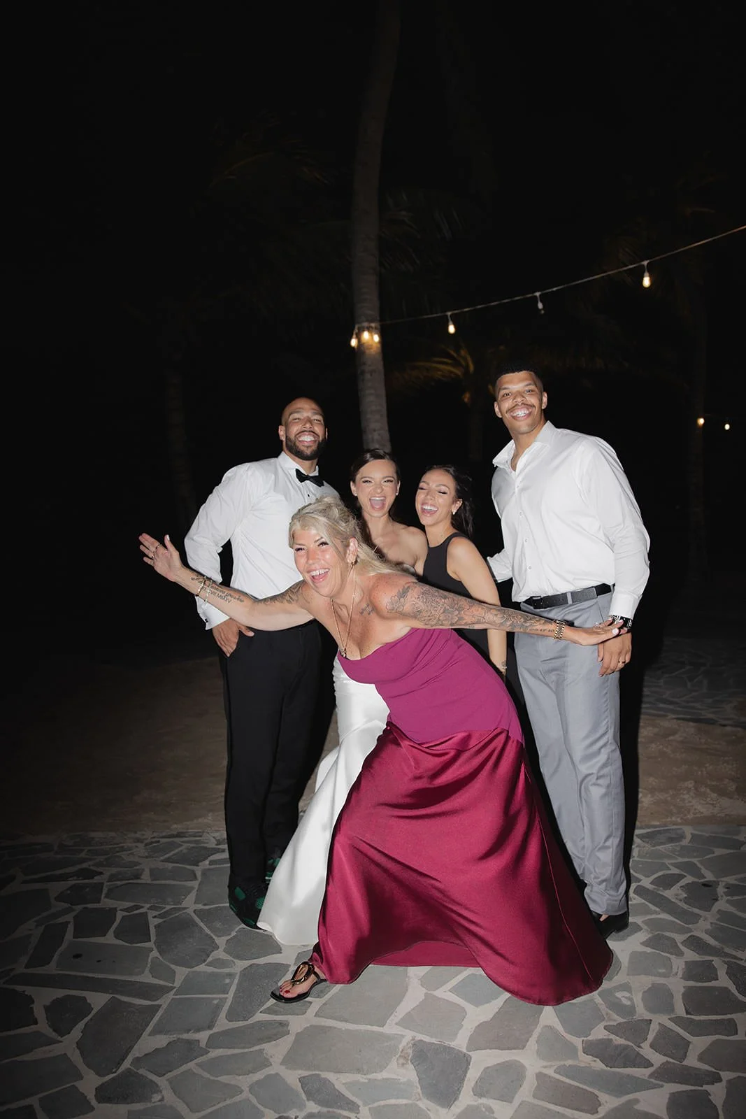 Wedding guests dancing outdoors at night under string lights, a guest in a dark pink dress striking a playful pose at the St. Lucia reception