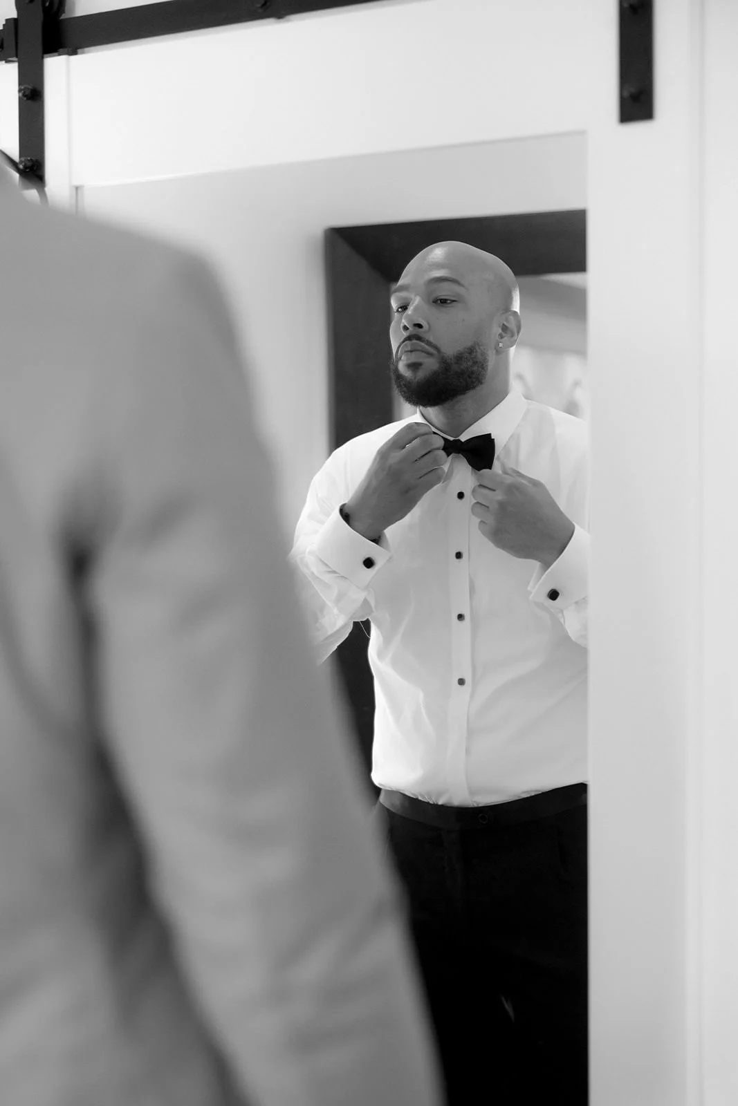 Black and white photo of the groom adjusting his bow tie in front of a mirror while getting ready in St. Lucia