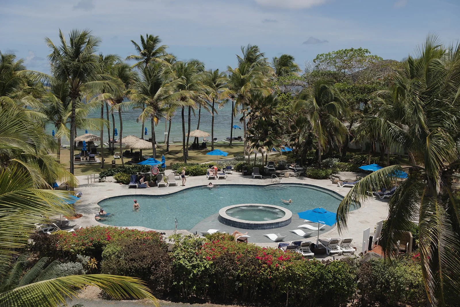 Wide view of the resort pool surrounded by palm trees and the ocean at Coconut Bay Beach Resort in St. Lucia