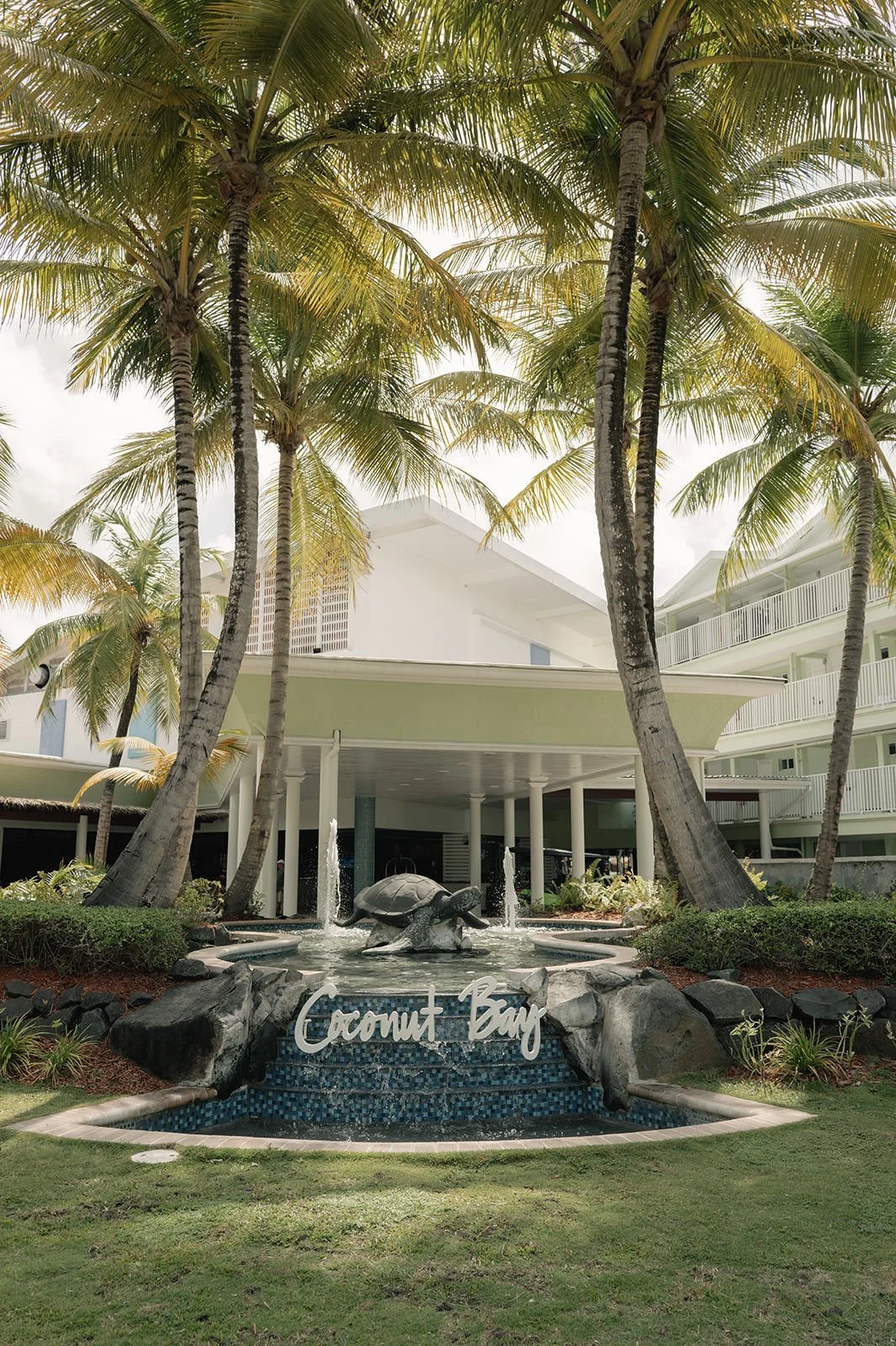 The Coconut Bay Beach Resort entrance fountain and sign framed by palm trees in St. Lucia