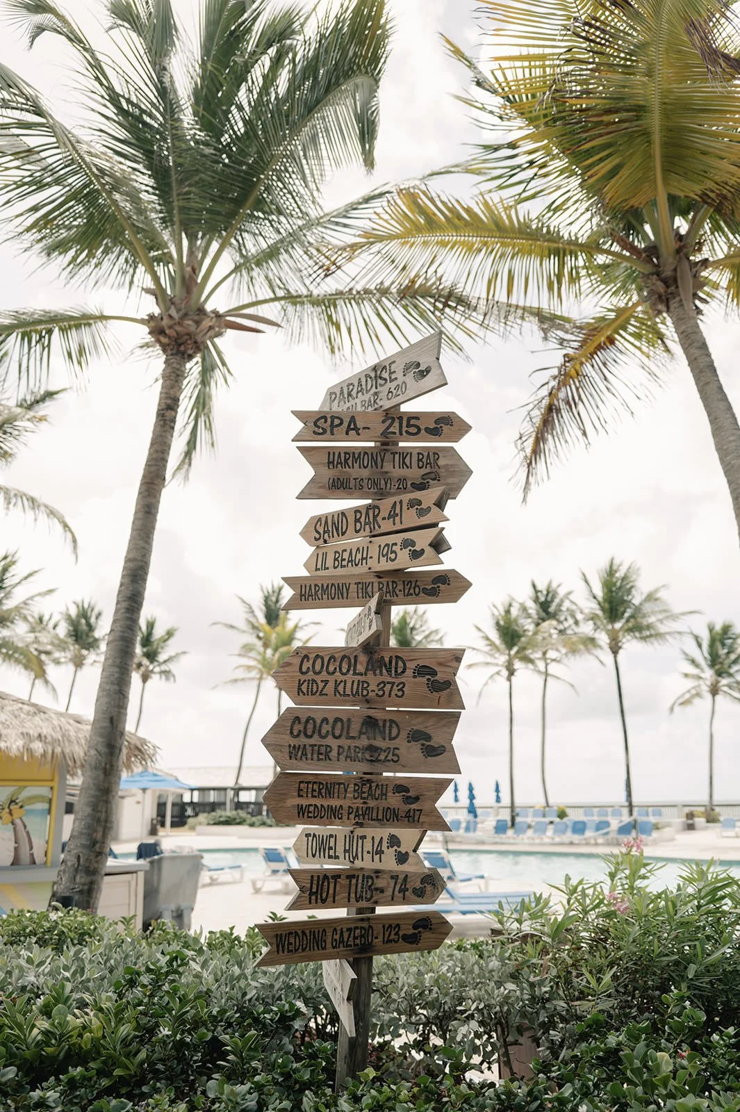 Wooden directional signpost pointing to resort locations among palm trees at Coconut Bay Beach Resort in St. Lucia