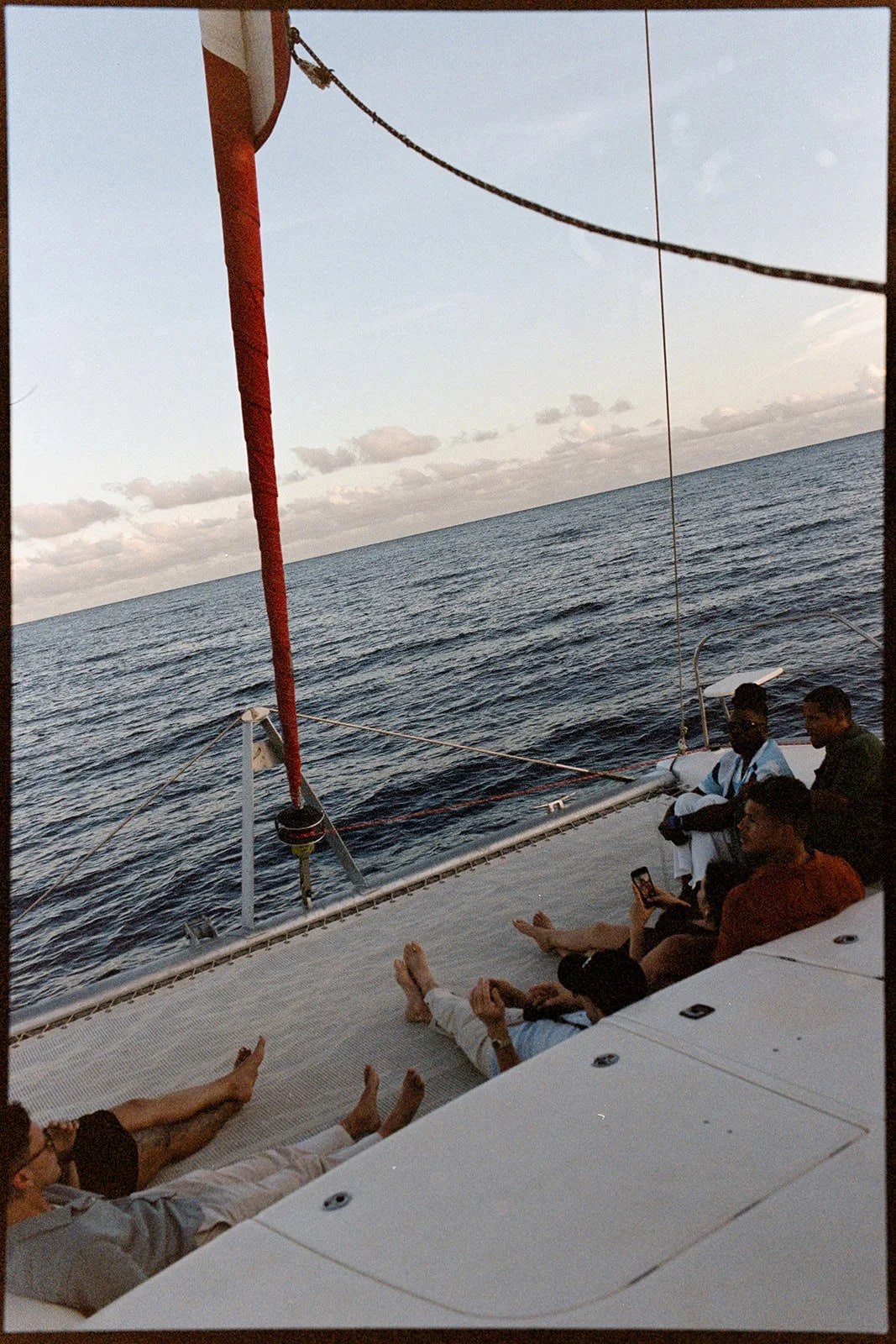 Wedding guests seated on the catamaran's deck beneath the red mast at sunset, St. Lucia coastline in the distance