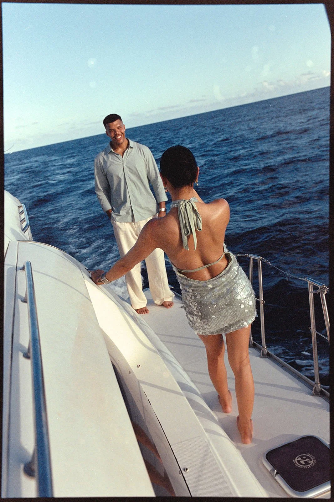 Groom and bride holding hands at the catamaran's railing, looking out over the water together during the sailing excursion