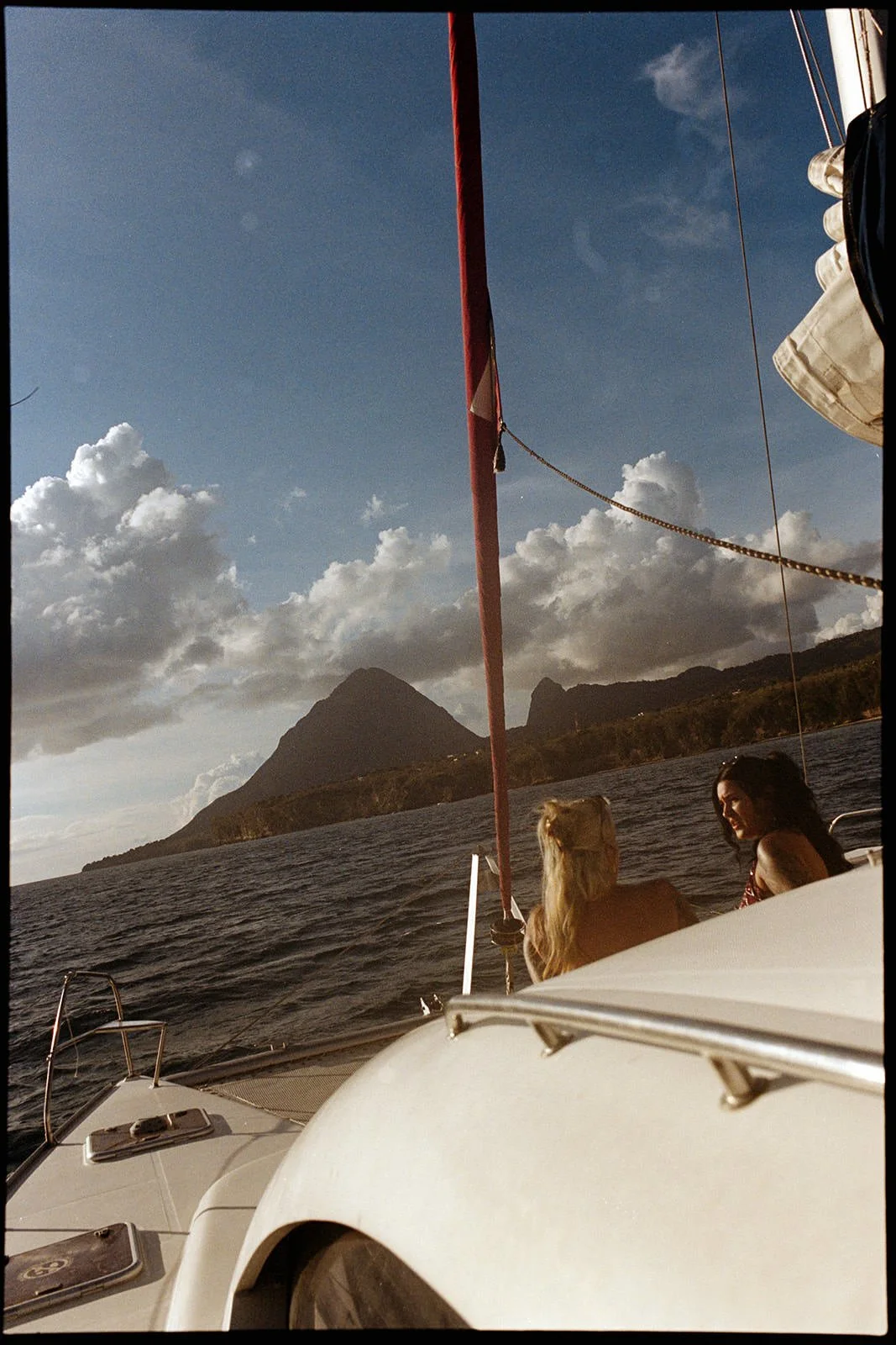 View of the catamaran's red mast against the sky with a St. Lucia mountain peak in the distance, guests seated below