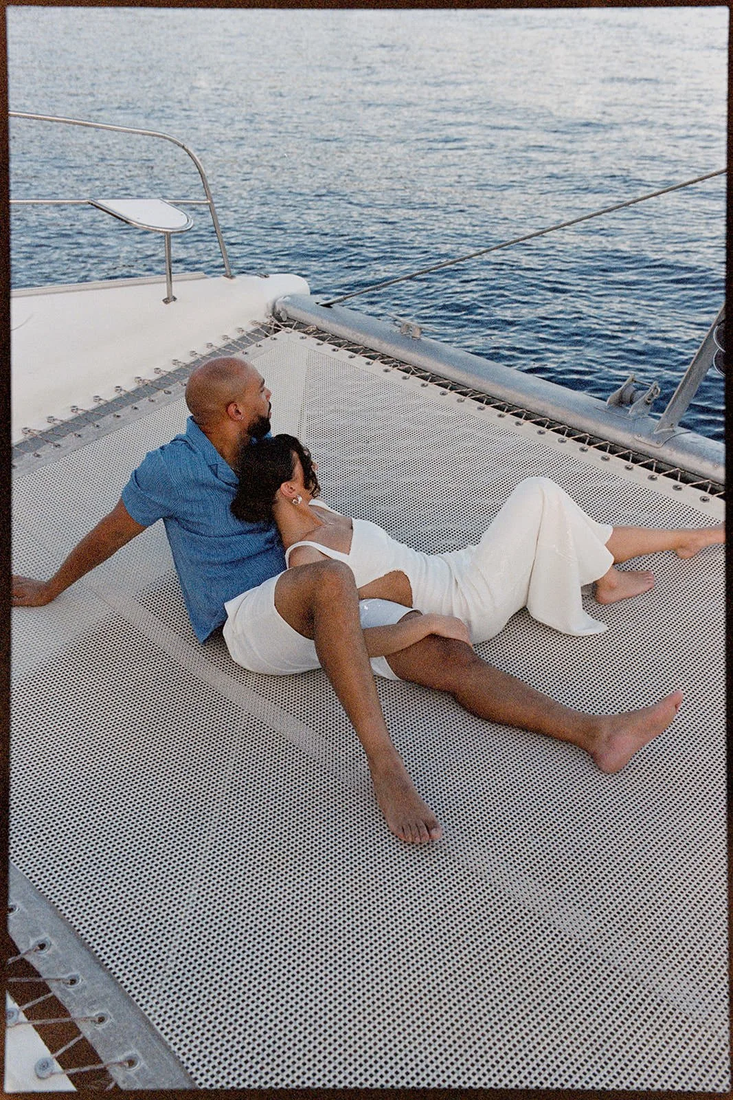 Groom and bride reclining together on the catamaran's trampoline netting, St. Lucia's coastline visible across the water