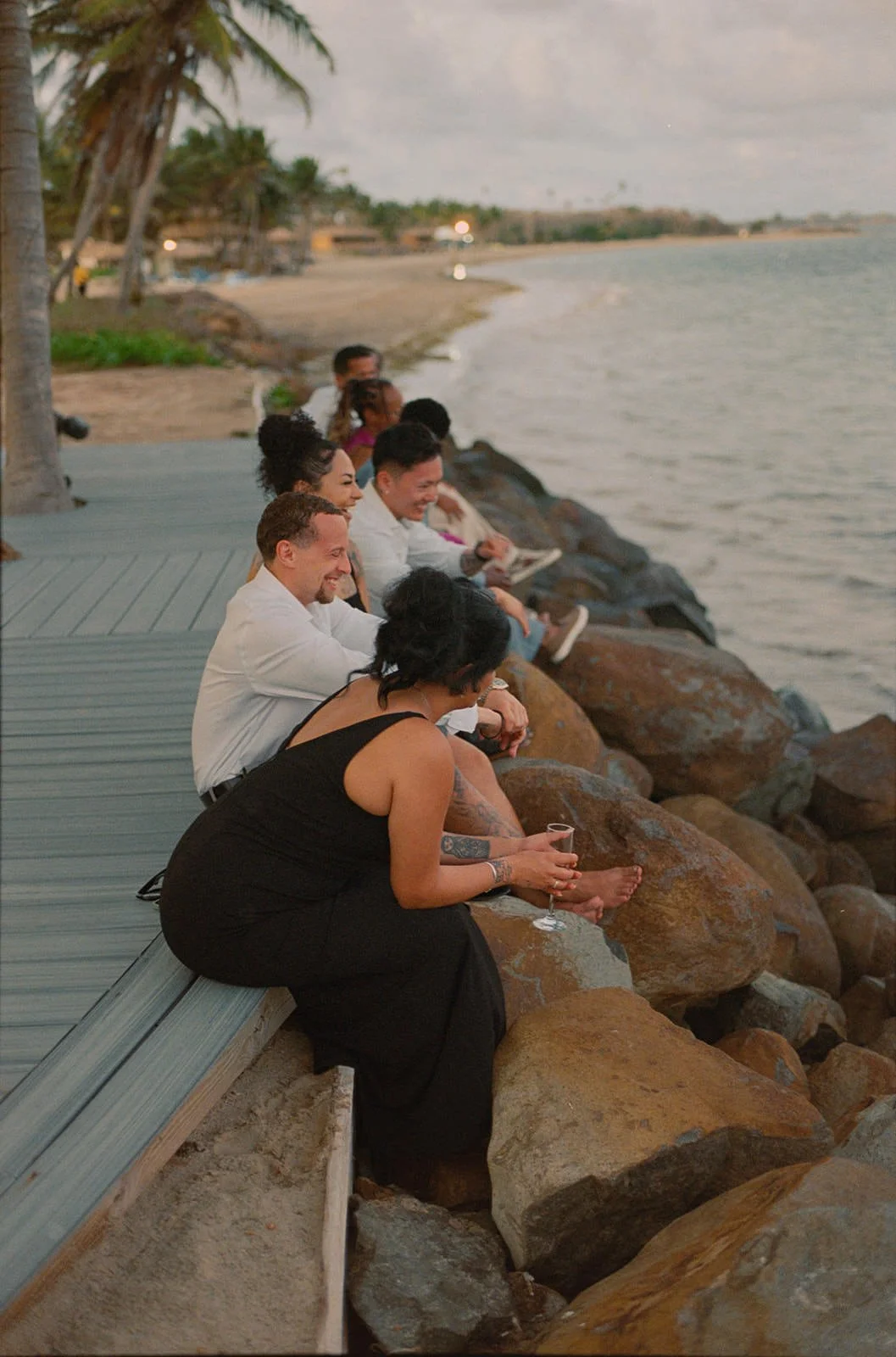 Wedding guests sitting together on rocks along the St. Lucia shoreline at dusk