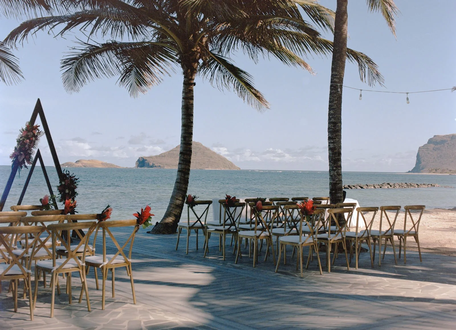 Beach reception setup with wooden tables and chairs between palm trees, ocean view before the St. Lucia celebration begins