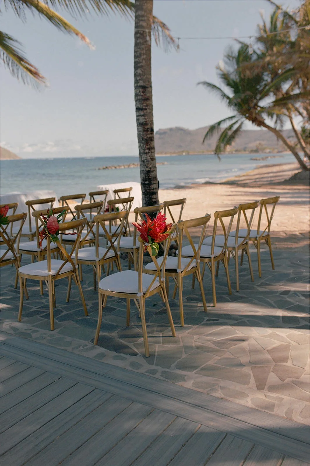 Rows of gold chairs set up for the St. Lucia beach ceremony, decorated with red floral centerpieces