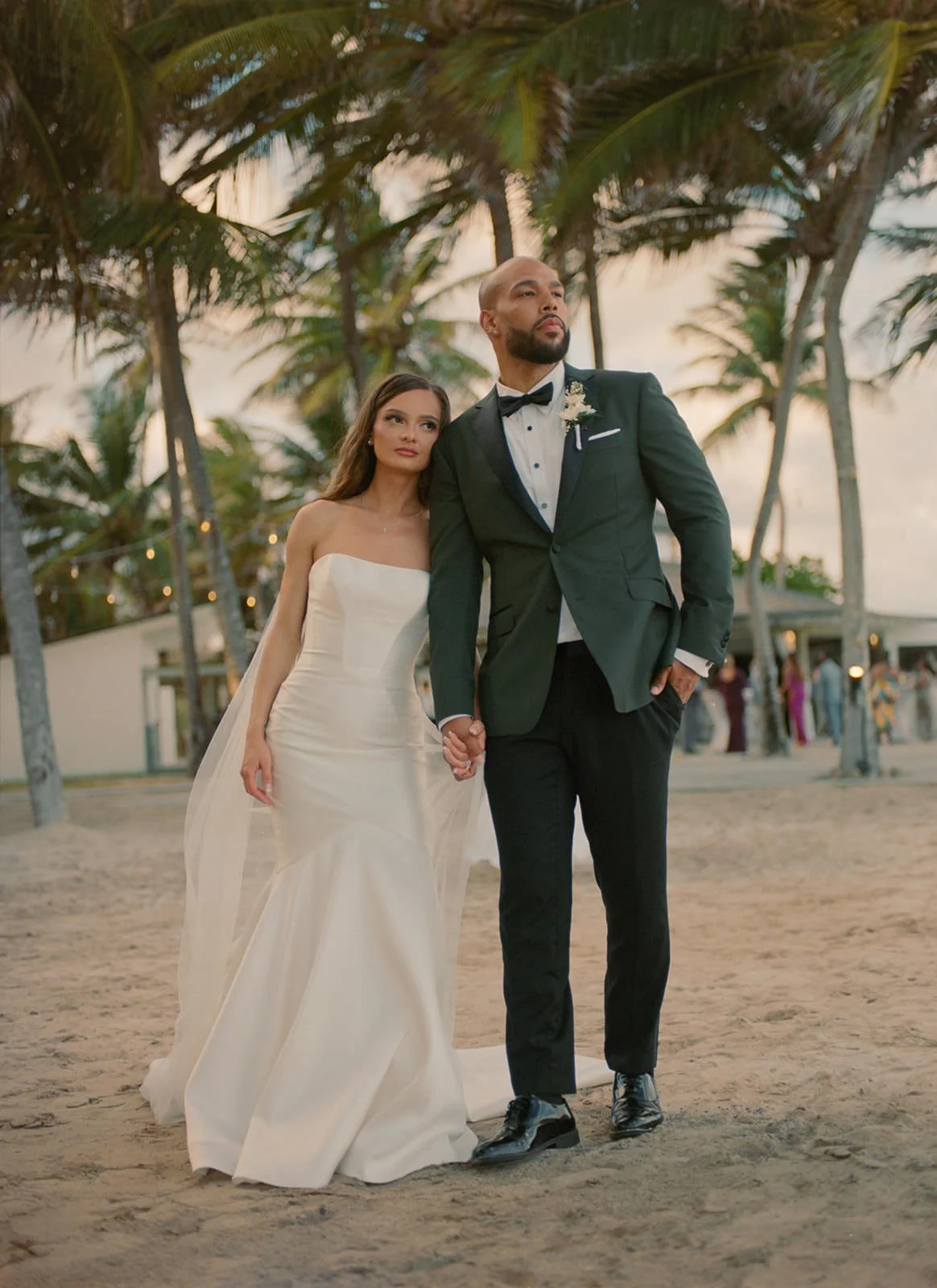 Bride and groom walking together hand in hand on the beach, palm trees lining the shore in St. Lucia