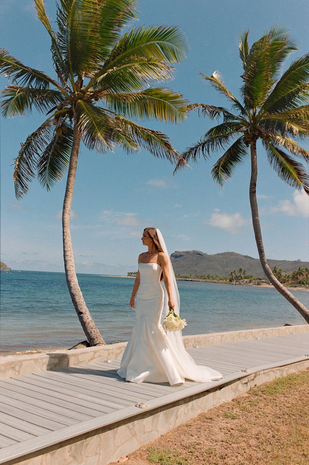Bride in a fitted gown walking along the boardwalk between palm trees at the St. Lucia wedding venue