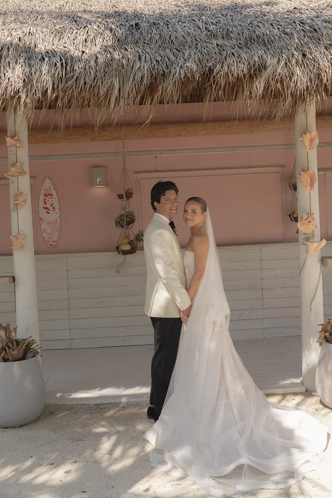 Bride and groom embrace on the beach beside the coral-pink cabana at the Islander Resort in Islamorada, Florida Keys