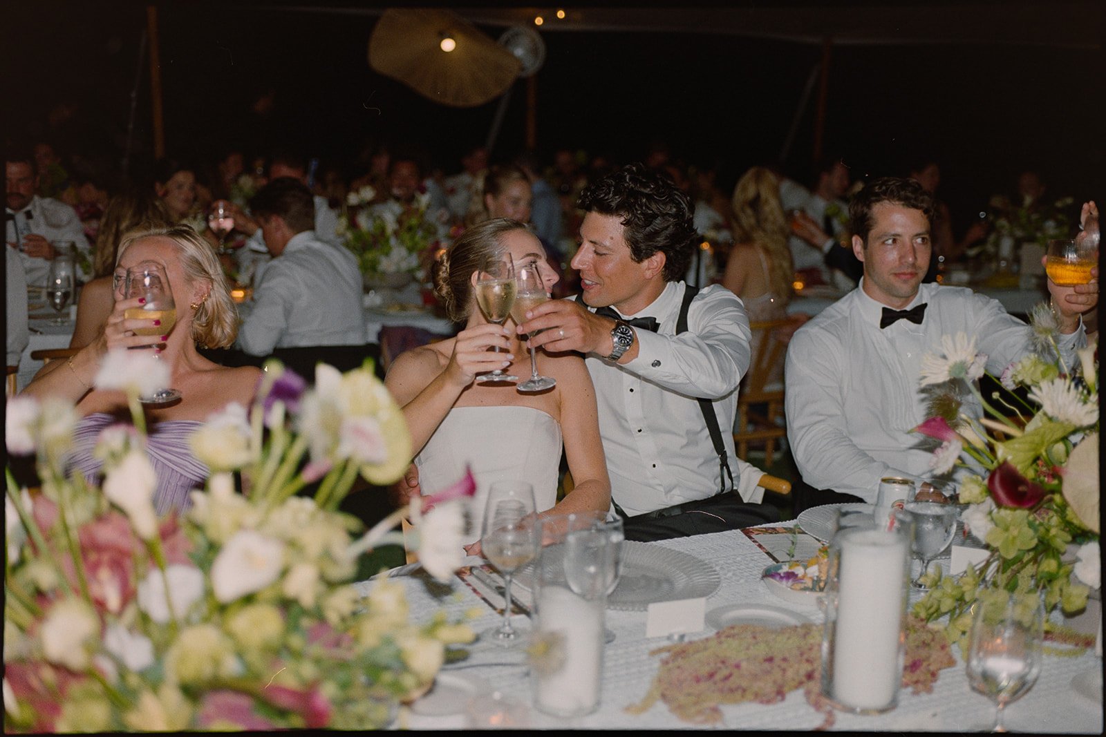 Guests toasting with drinks at the banquet table decorated with florals at the reception for this Islamorada, Florida Keys destination wedding