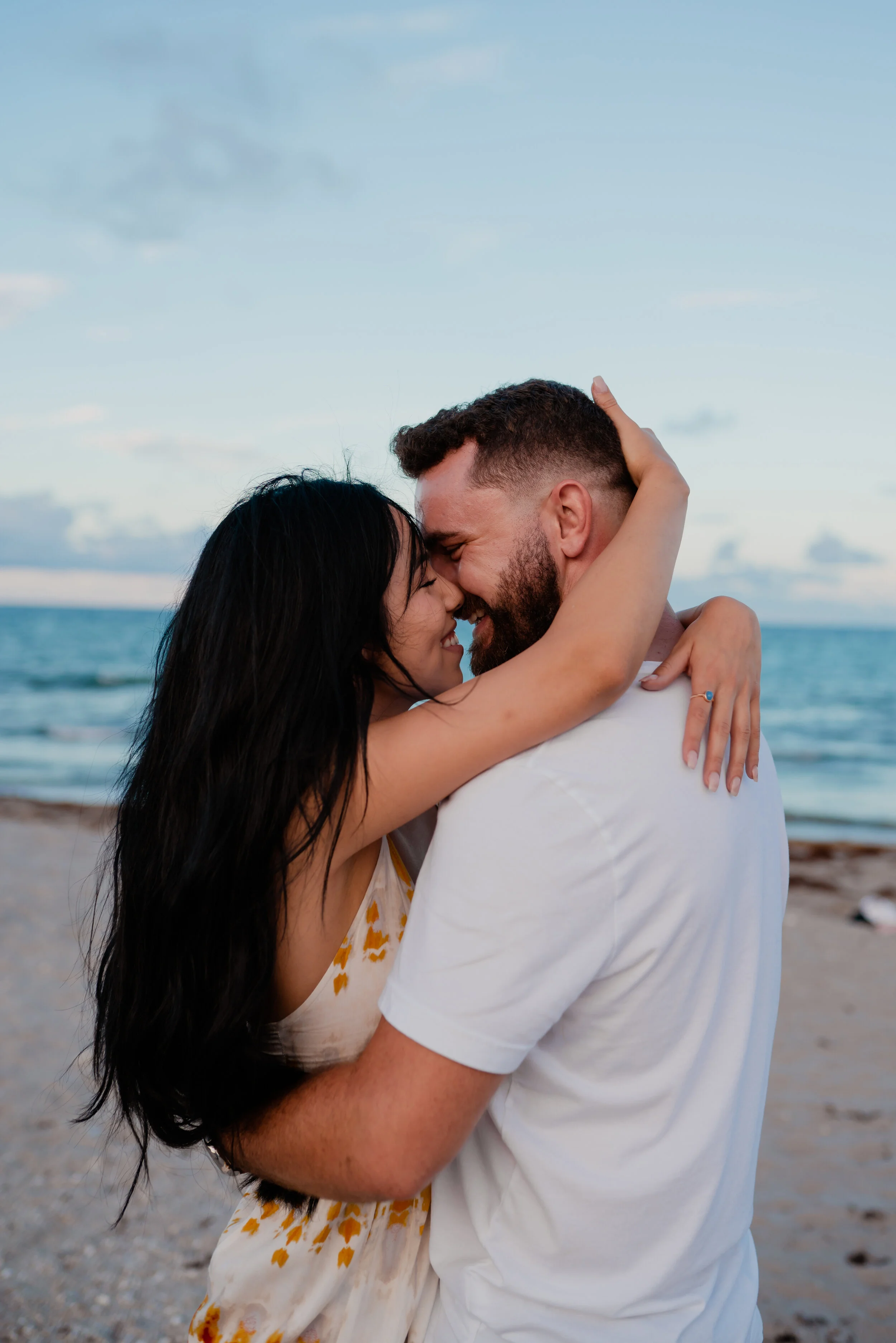 A couple hugging and smiling on the beach during sunset.