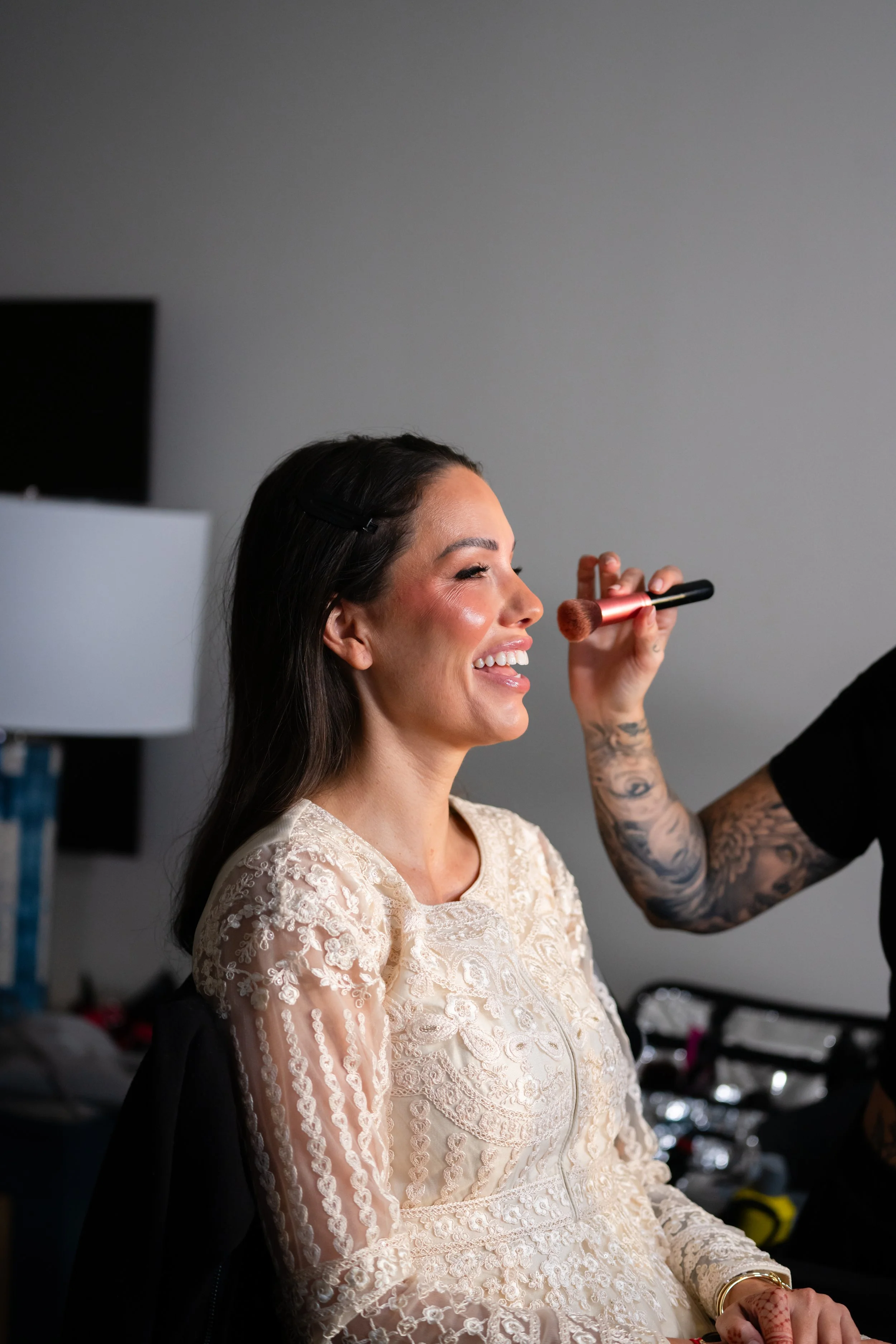 Woman getting her makeup done, smiling while a makeup artist applies blush with a brush.