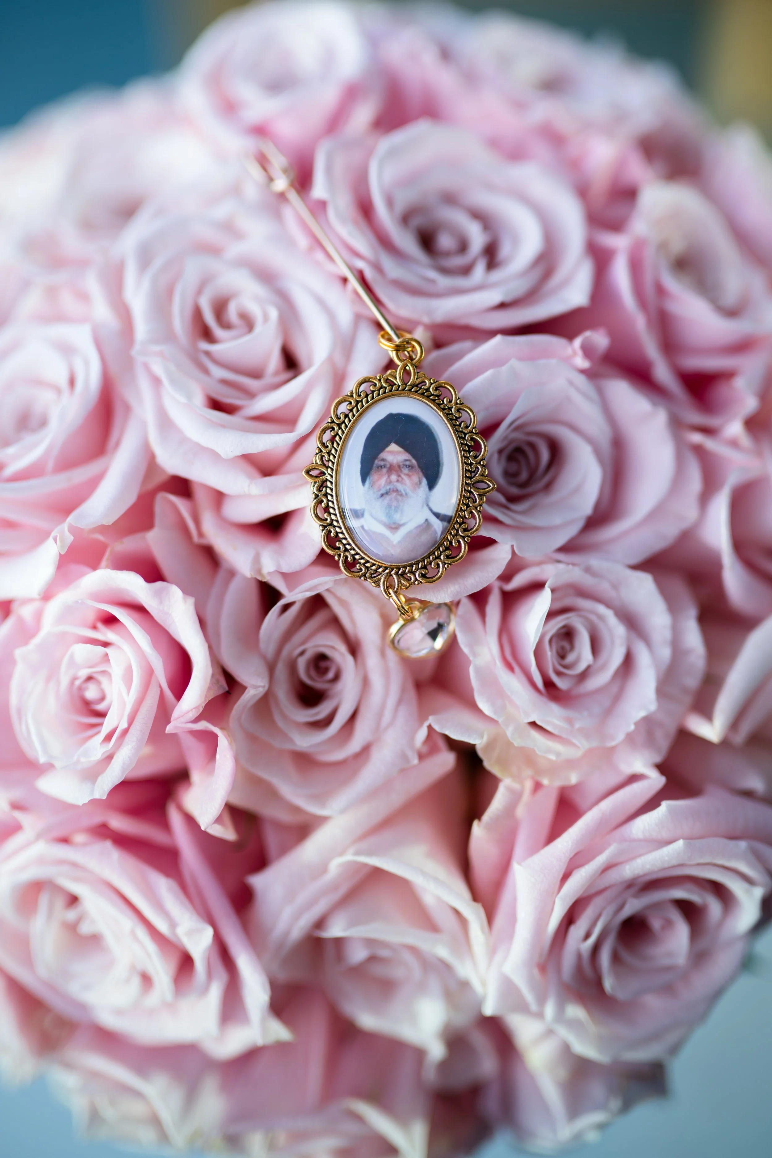 A gold ornate necklace with a photograph of a Sikh man with a turban and beard, resting on a bouquet of light pink roses.