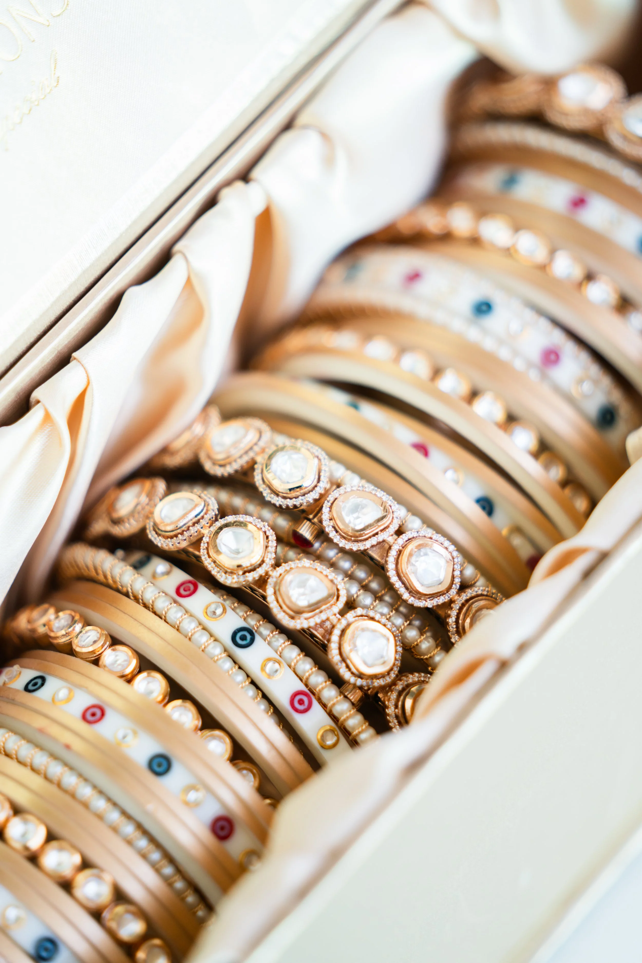 A jewelry box filled with gold and pearl bracelets, some with clear gemstones, and decorative colored beads on a cream-colored fabric lining.