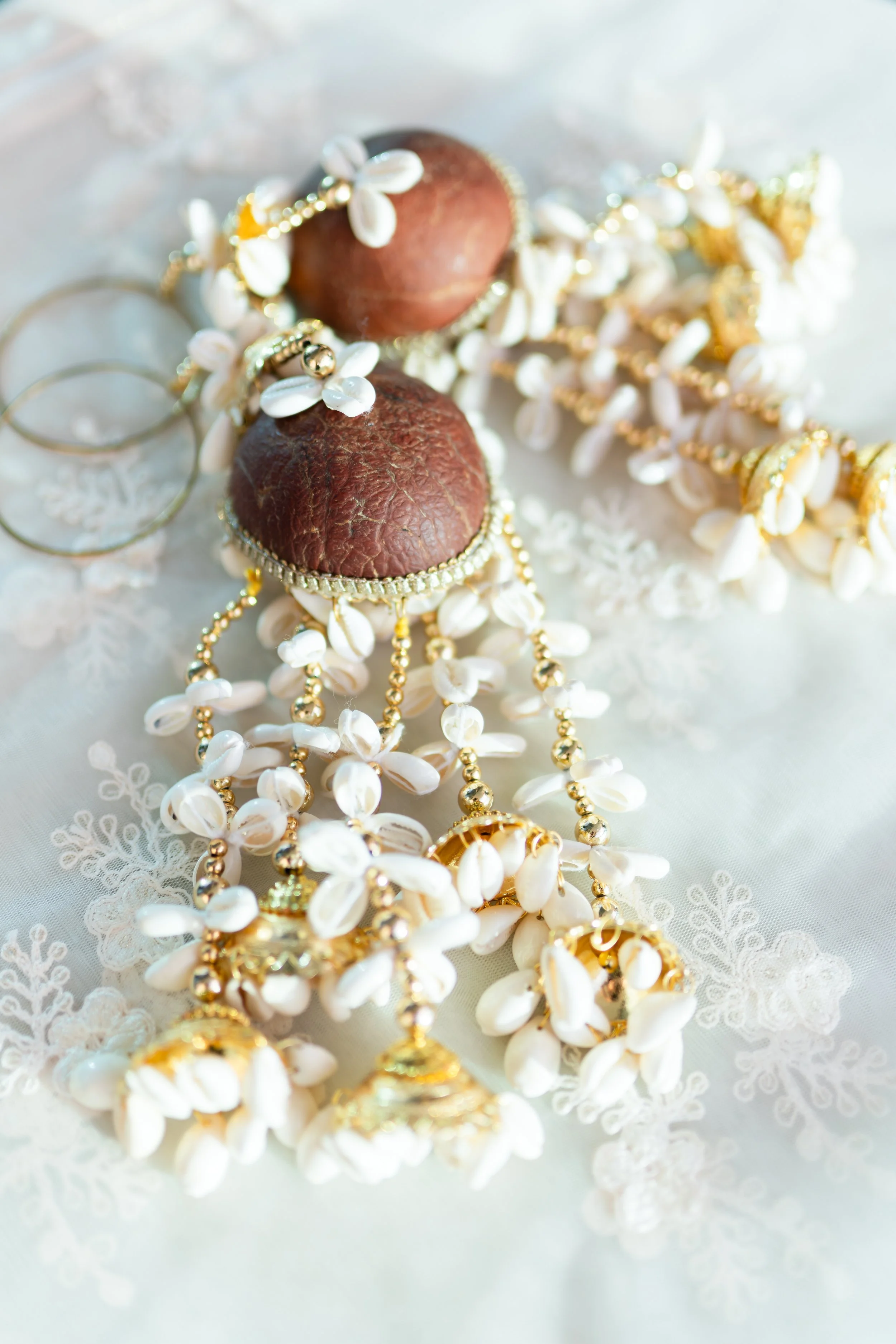Close-up of pearl and gold jewelry with brown seashells on a white lace surface.
