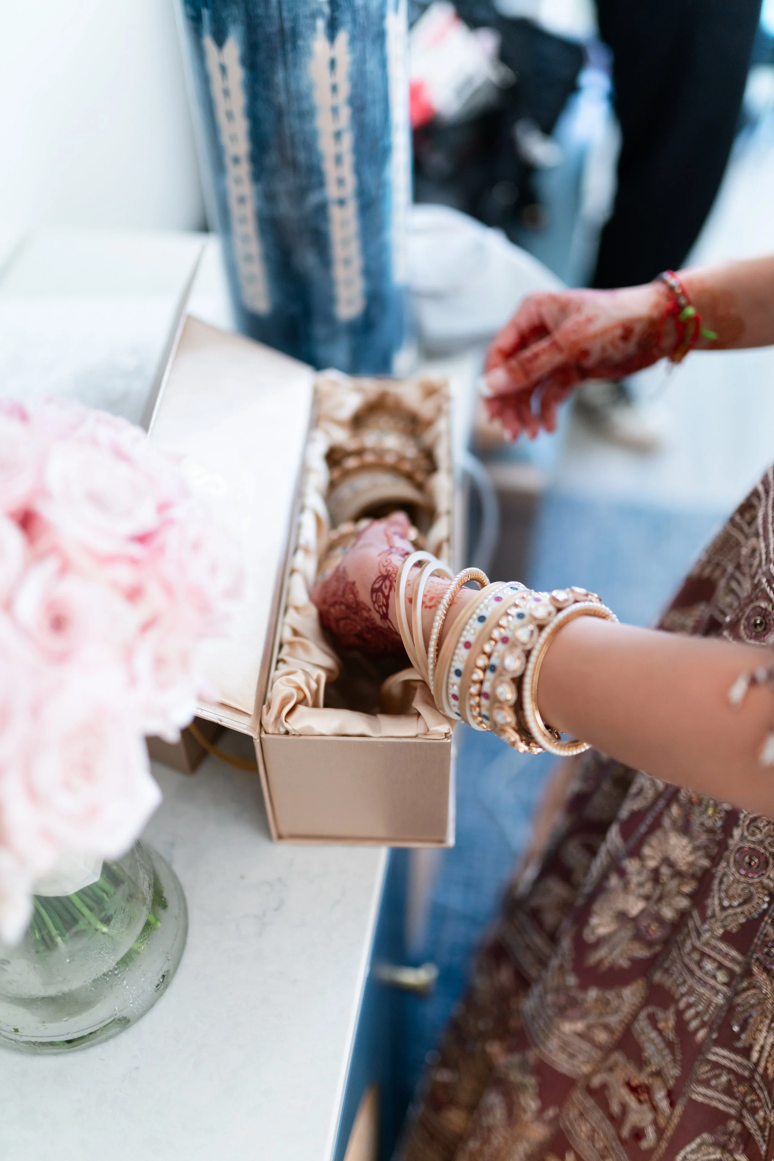 A woman selecting jewelry from a box, wearing multiple bangles, in a retail or jewelry store.