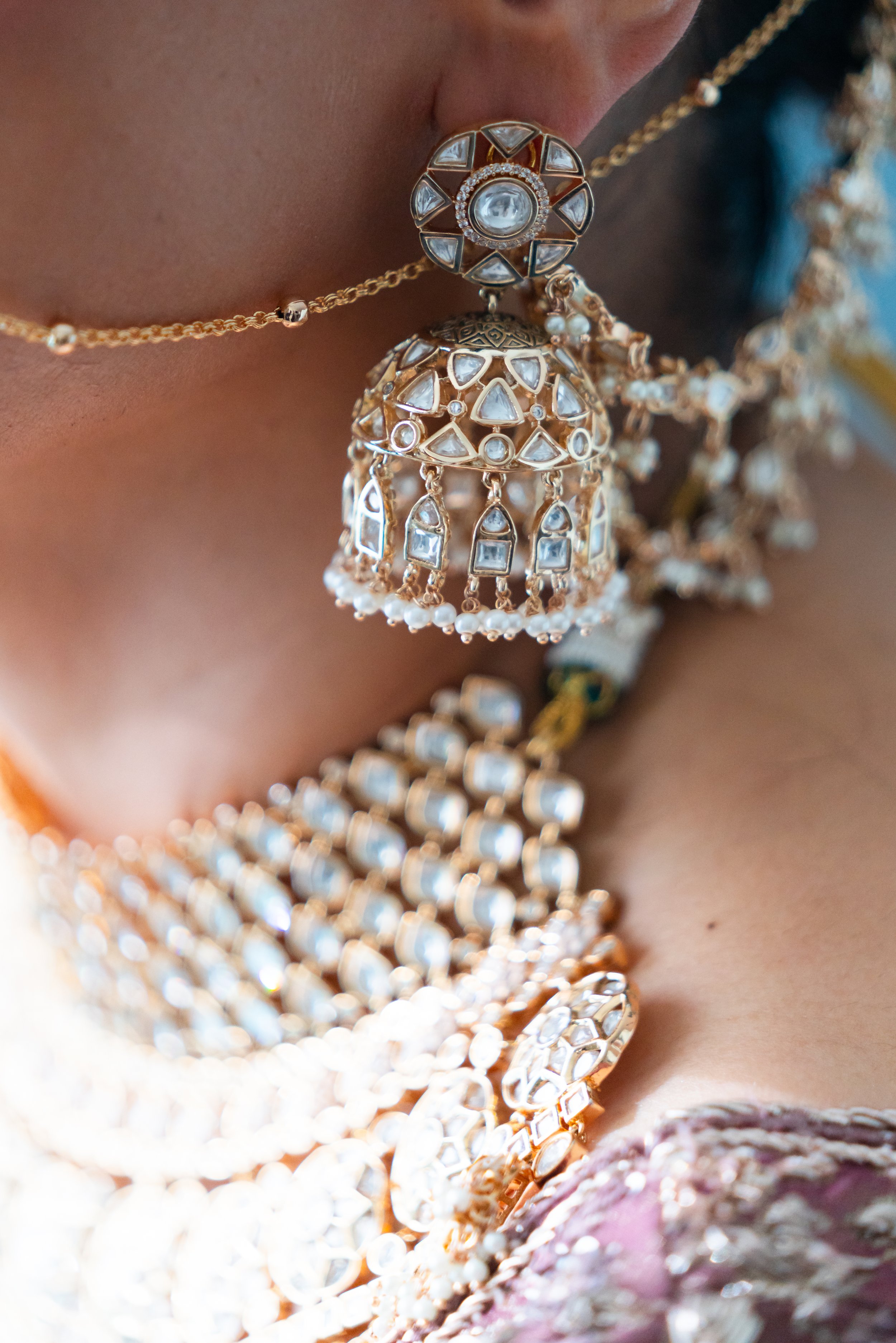 Close-up of a person wearing traditional gold jewelry with intricate designs, including large earrings, layered necklaces, and a chain around the neck.