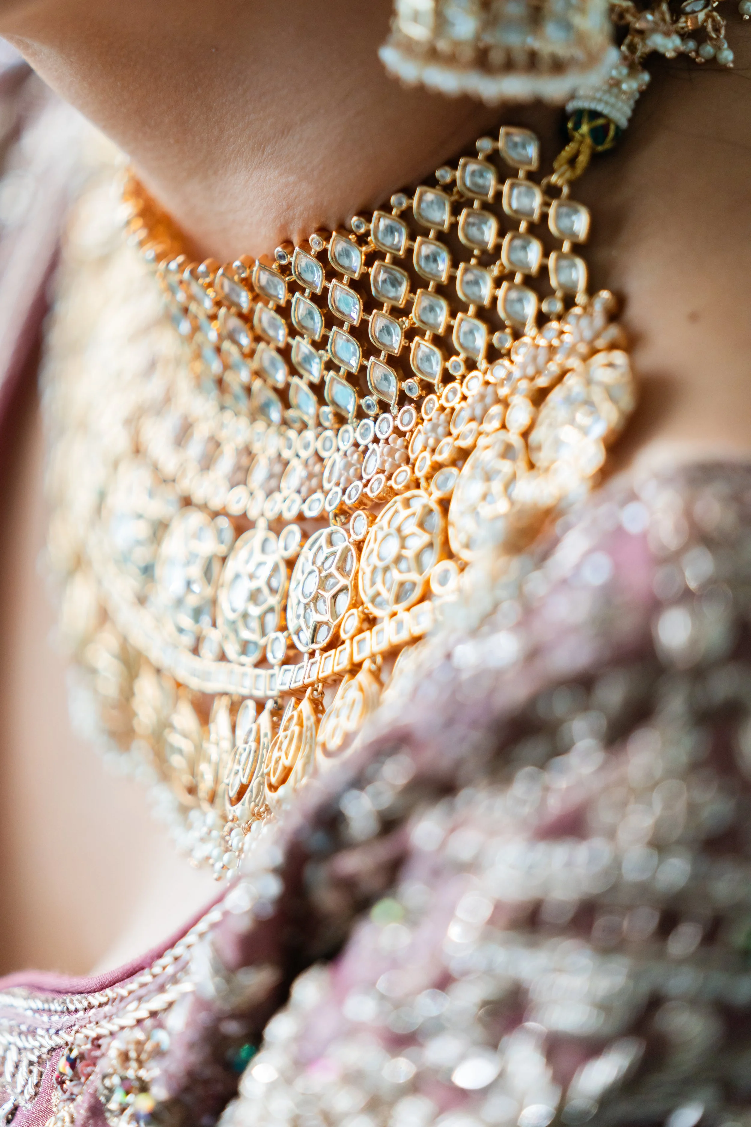Close-up of layered gold and diamond necklaces worn on a person's neck, with a pink and silver embroidered fabric visible.