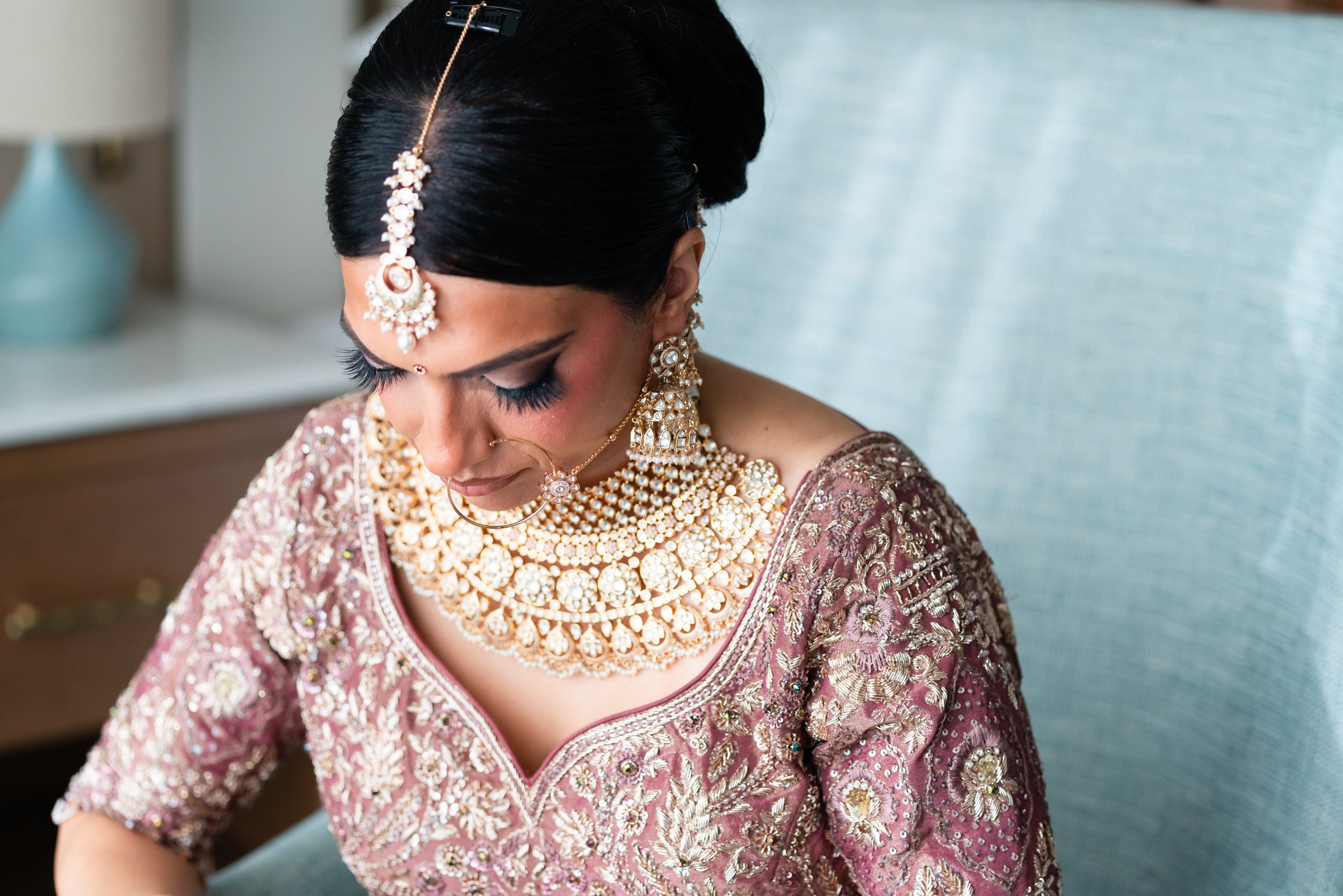 A woman dressed in traditional Indian bridal attire, wearing intricate gold and pearl jewelry, with her hair styled elaborately.