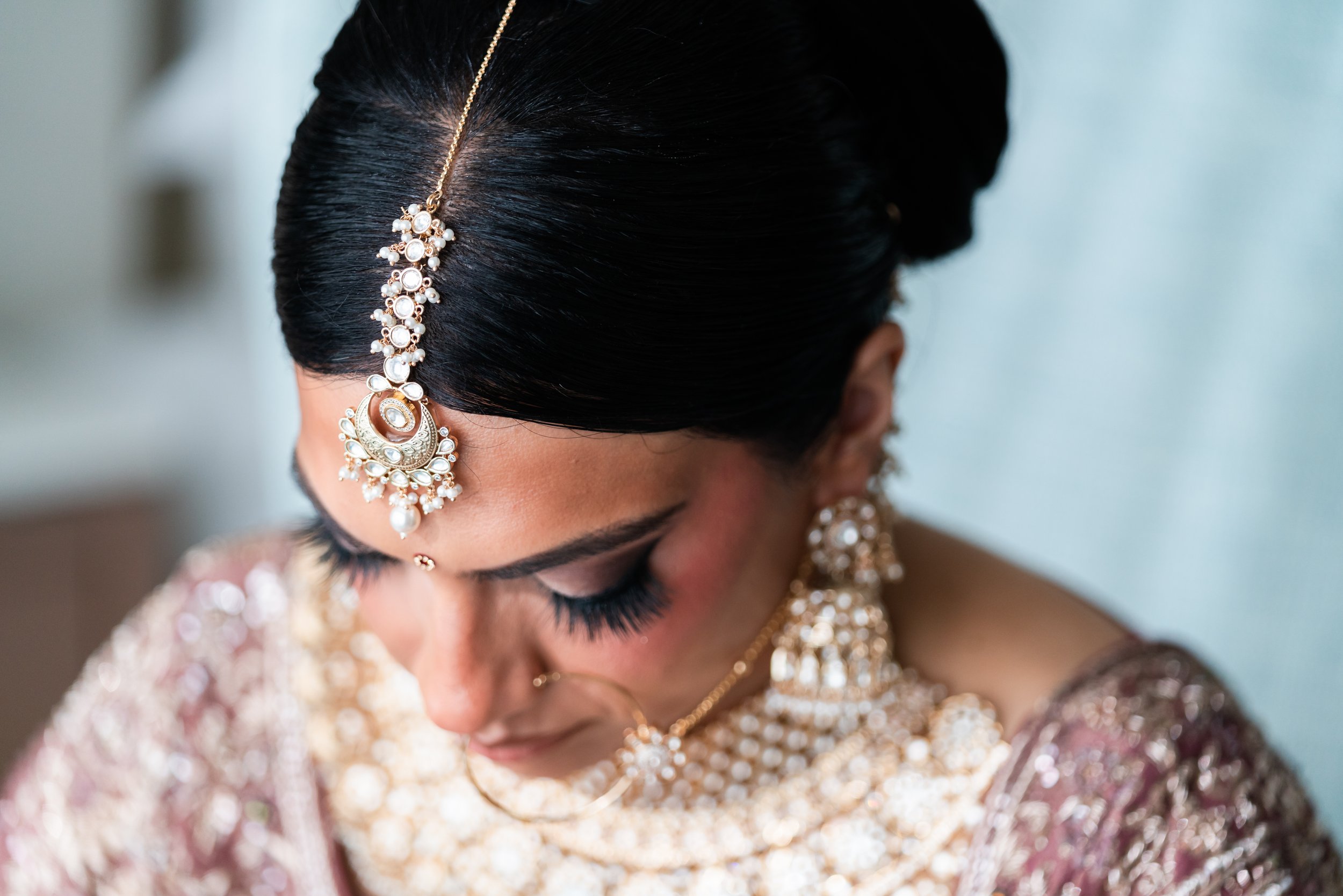 Close-up of a woman dressed in traditional bridal attire, wearing intricate jewelry including a maang tikka, earrings, and necklaces with black hair styled in an elegant updo.