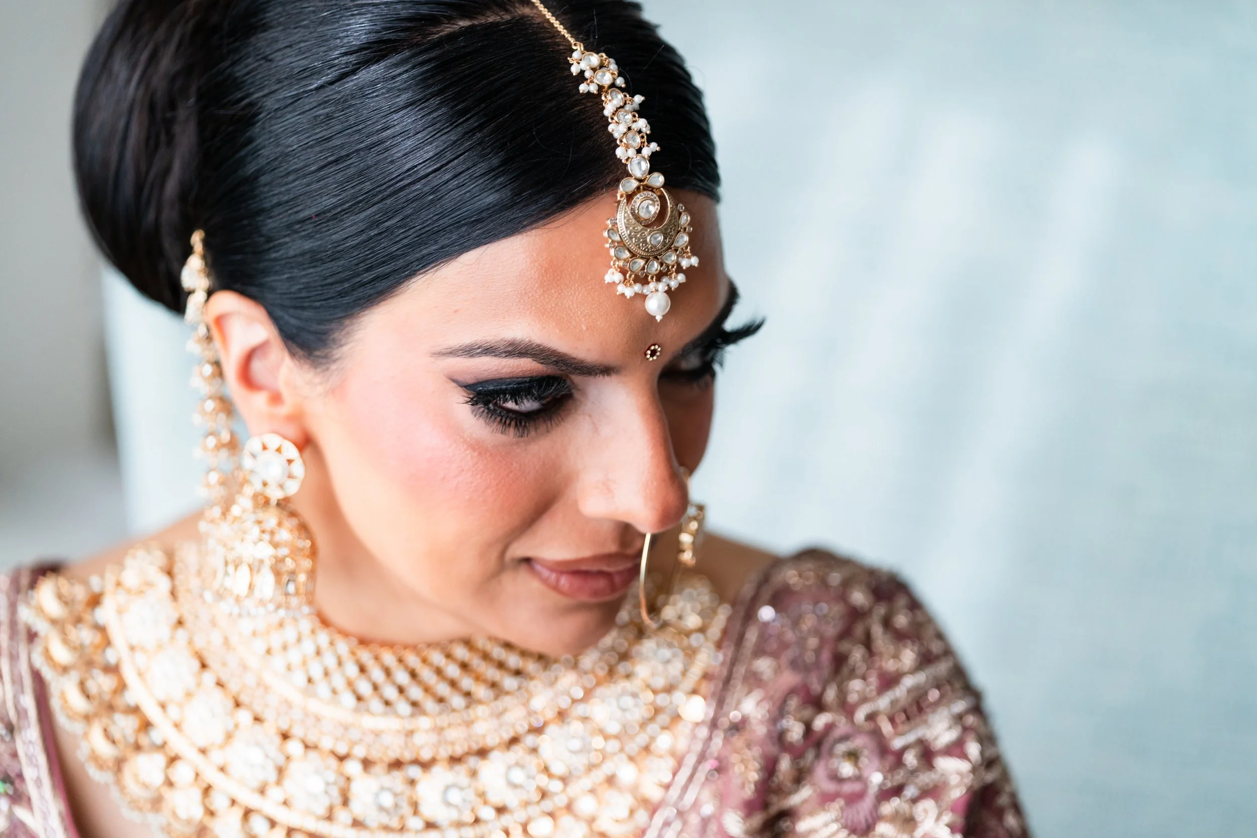 Close-up of a woman dressed in traditional Indian attire with elaborate jewelry, including earrings, necklaces, a maang tikka, and a nose ring. South Florida Wedding Photographer, Manhattan Wedding Photographer, Wedding Photographer