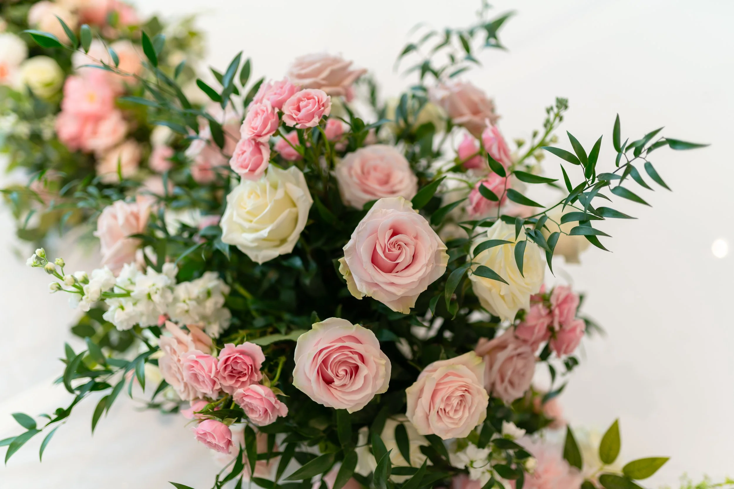 A bouquet of pink and white roses with green leaves and small white flowers.