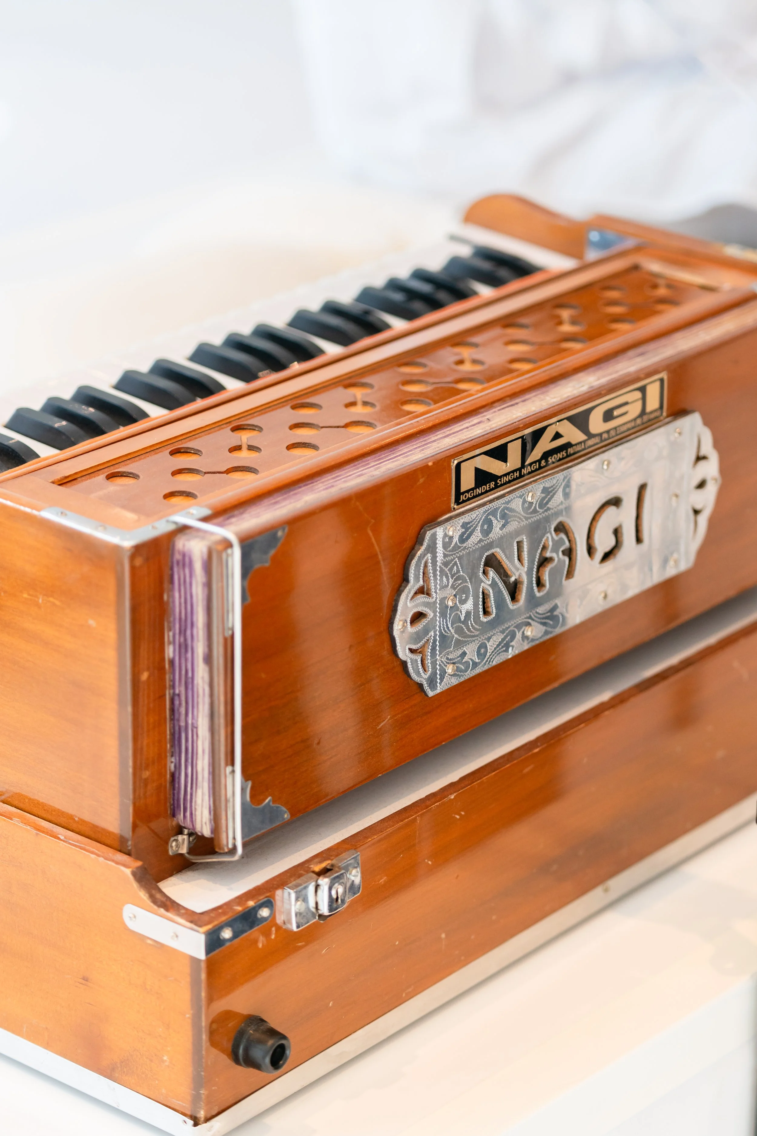 A wooden harmonium with black and white keys, a metal nameplate, and musical holes on top