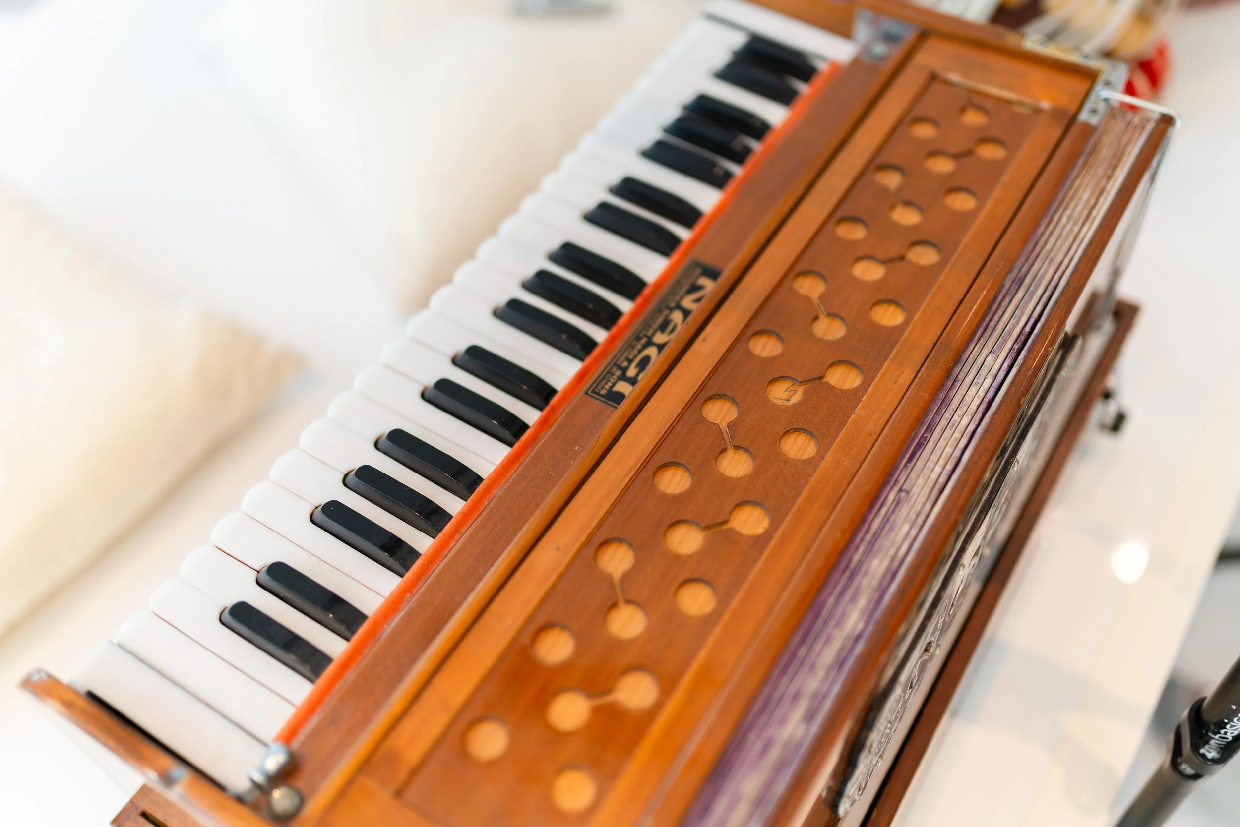 A vintage wooden harmonium with black and white keys and circular holes on the top, placed on a white surface.