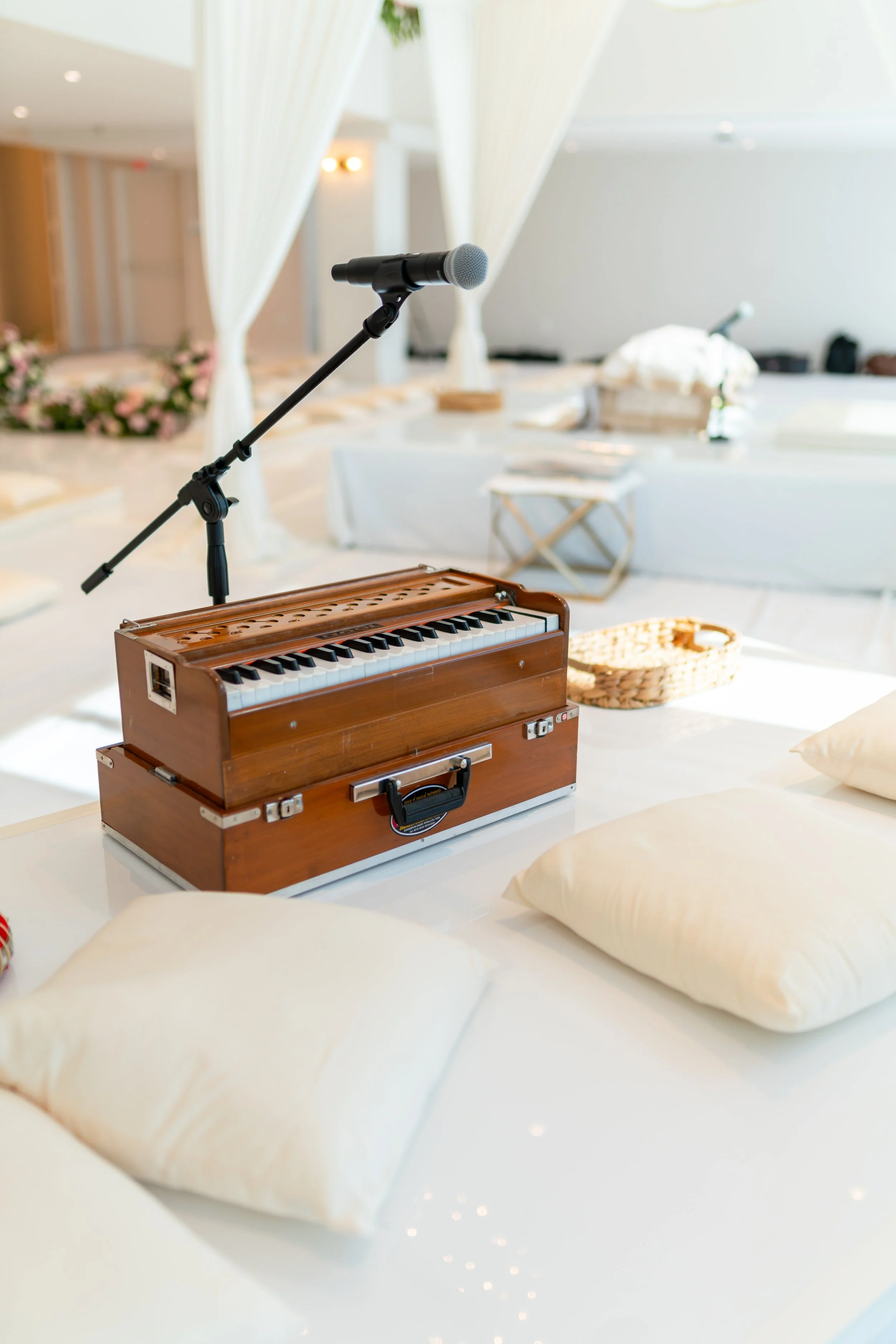A miniature wooden piano with a microphone on a stand in a bright, decorated room with white draped curtains and pillows.