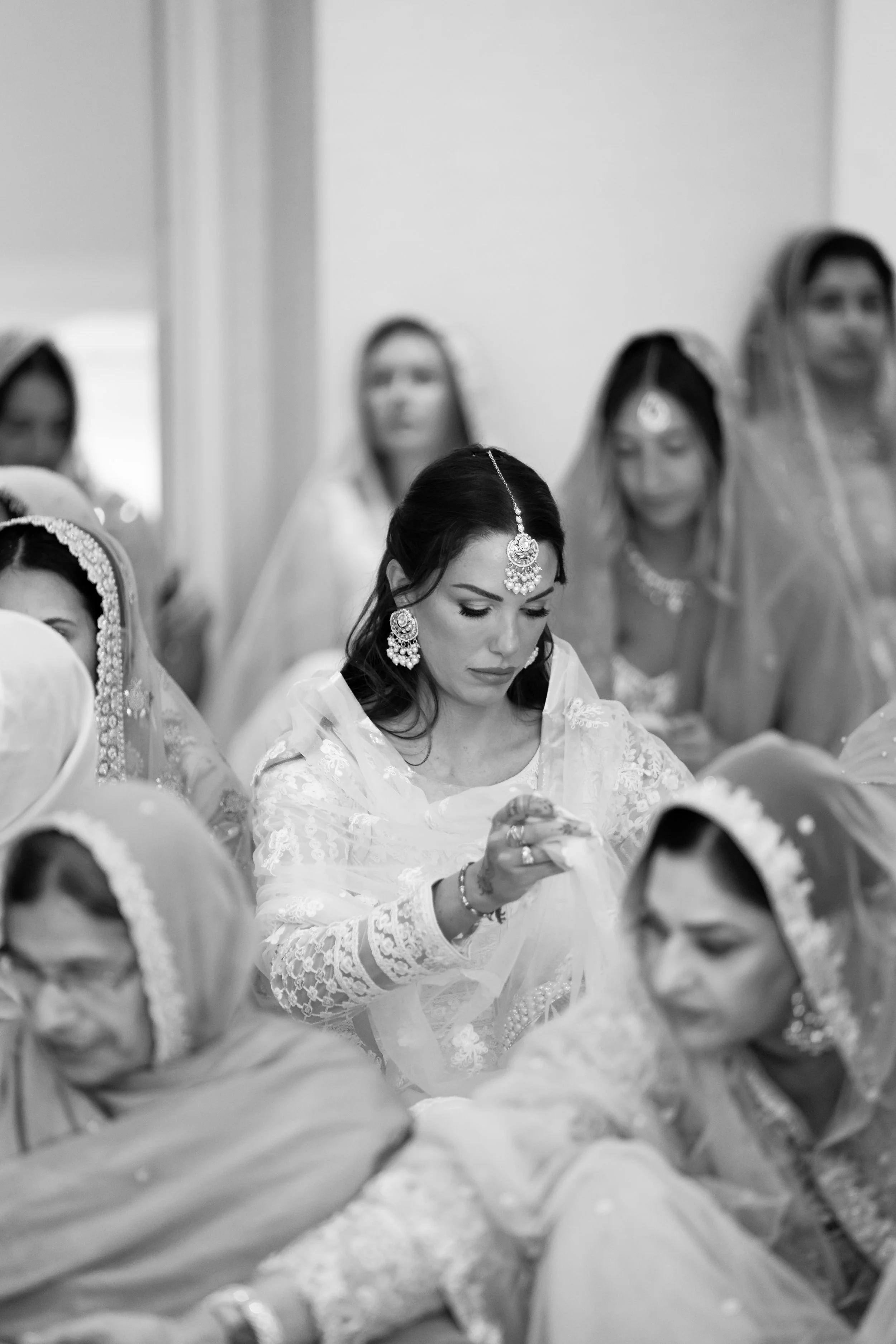 A woman dressed in traditional Indian attire and jewelry participating in a wedding ceremony, surrounded by other women also in traditional dresses.