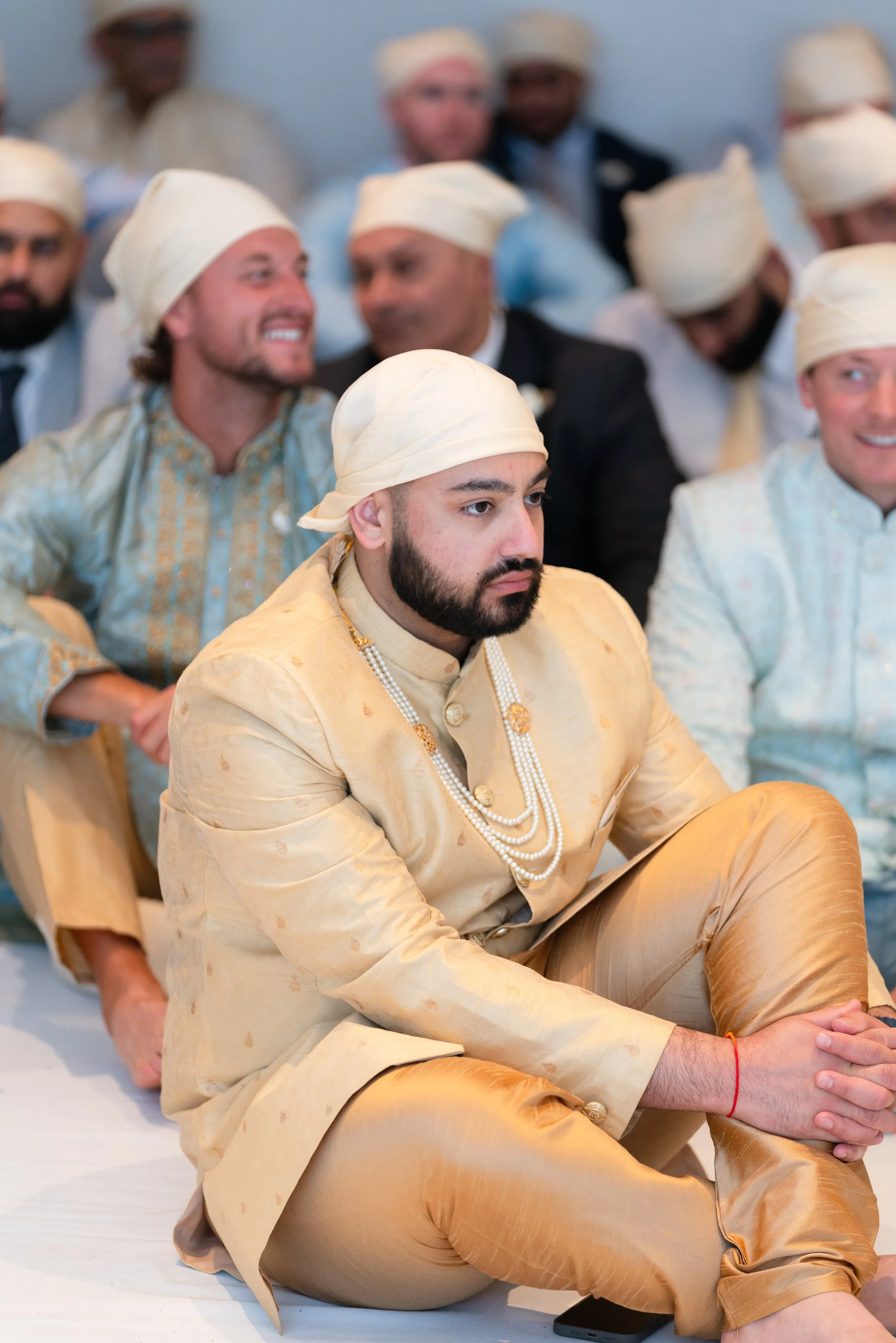 Group of men wearing traditional Indian attire and head coverings, sitting attentively at an event.
